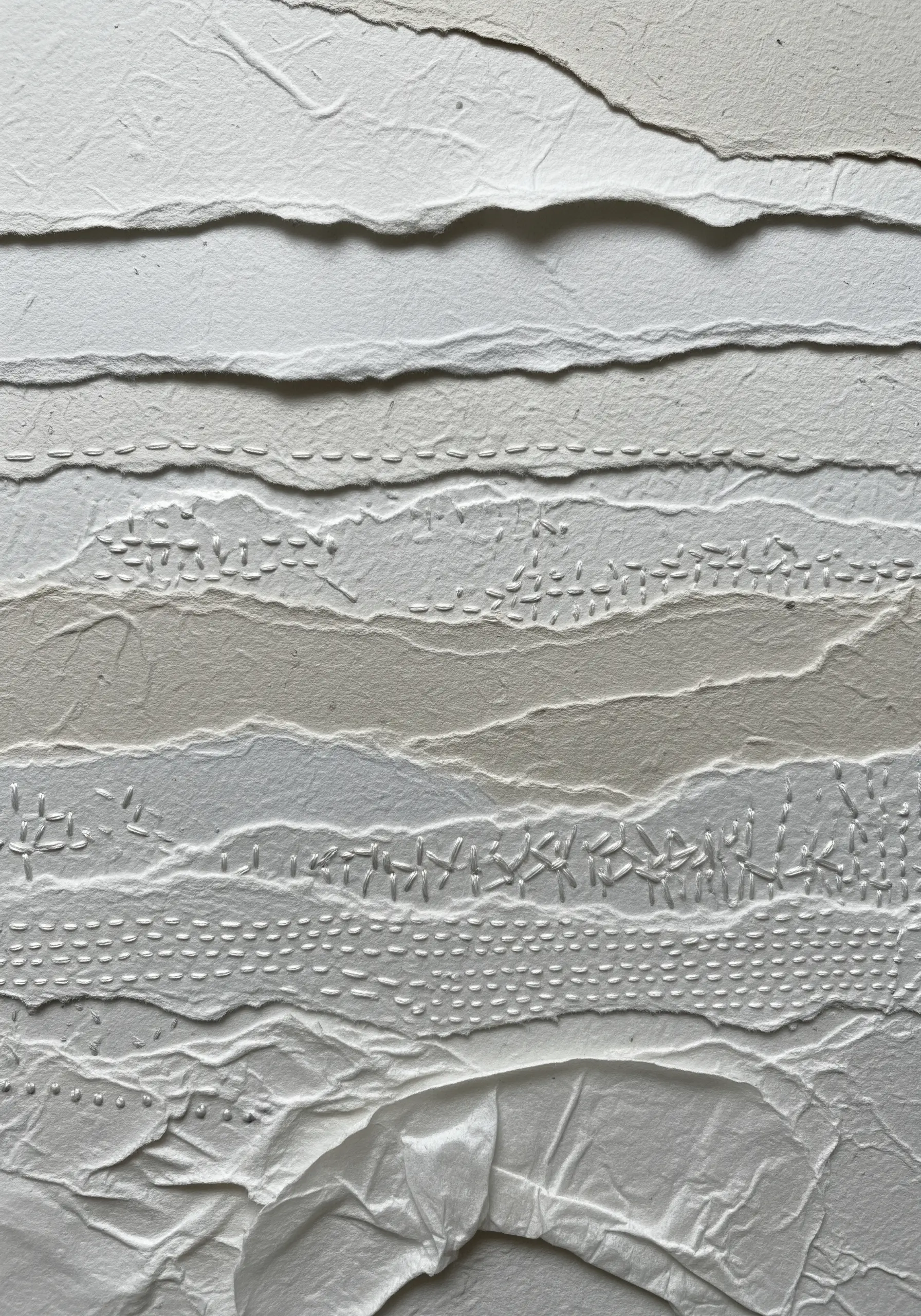 A white-on-white collage of torn paper with various subtle white embroidery stitches for texture.