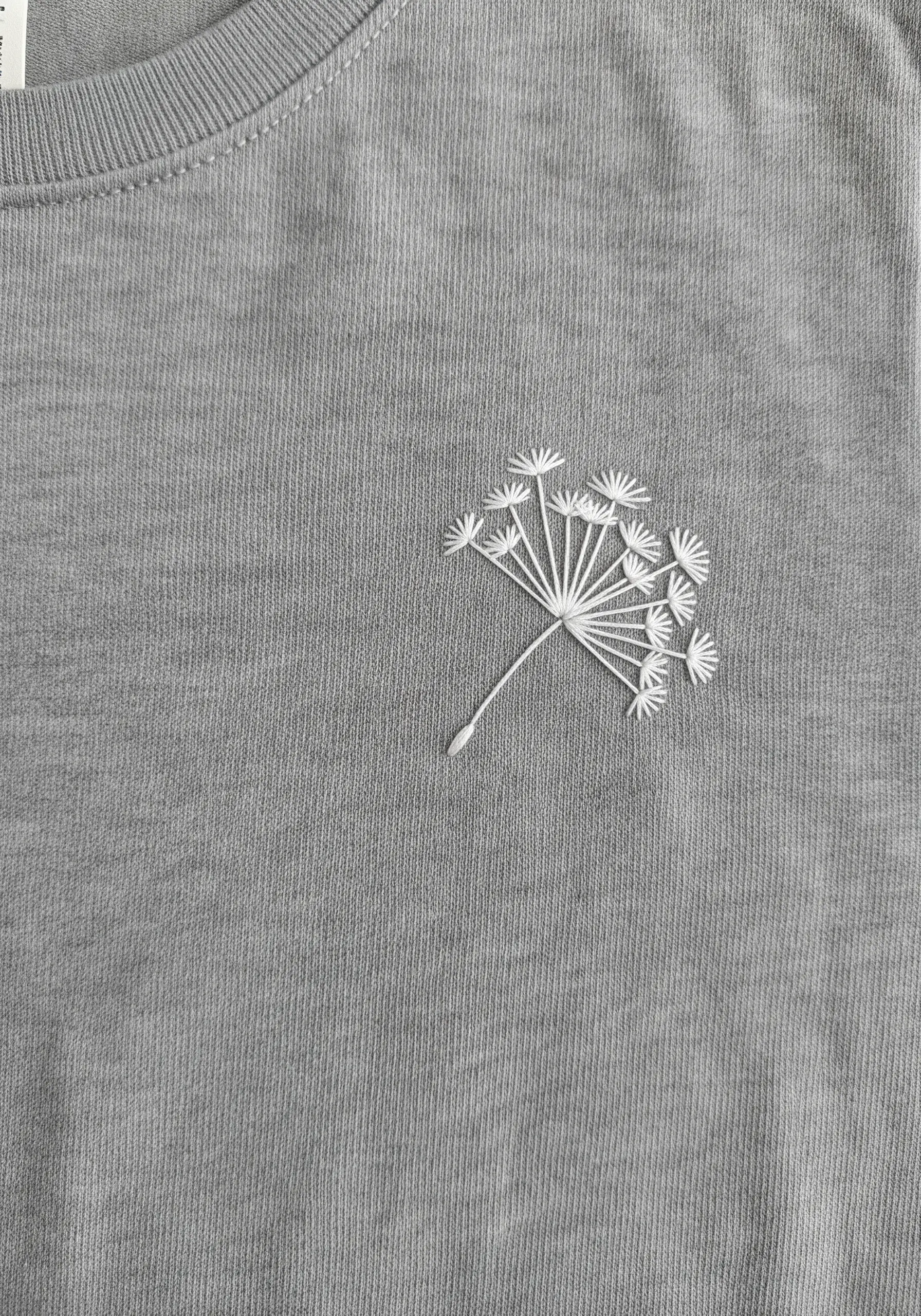 White dandelion seed head embroidered on a light grey t-shirt.