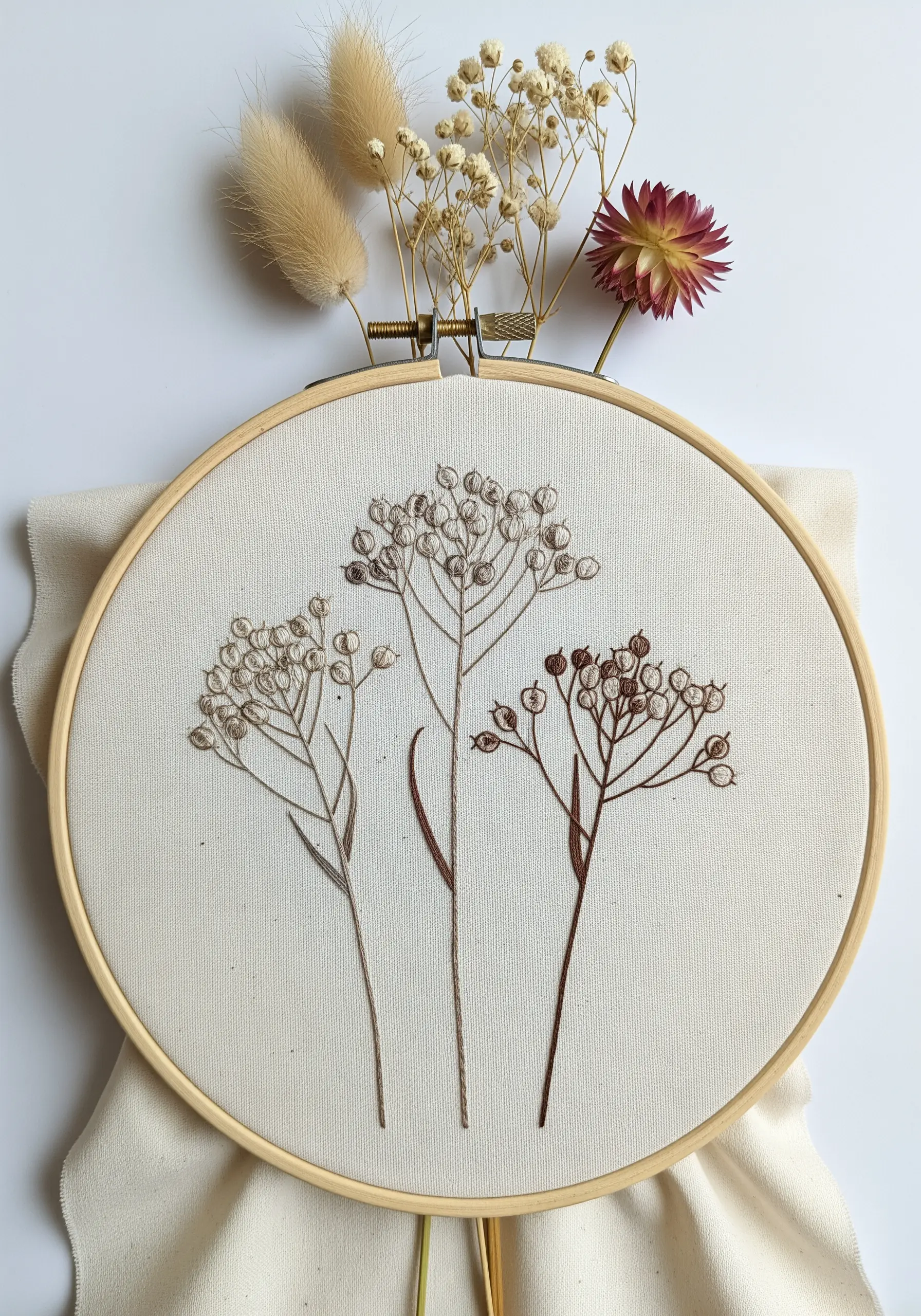 Delicate monochrome embroidery of dried seed pods and branches on off-white fabric.