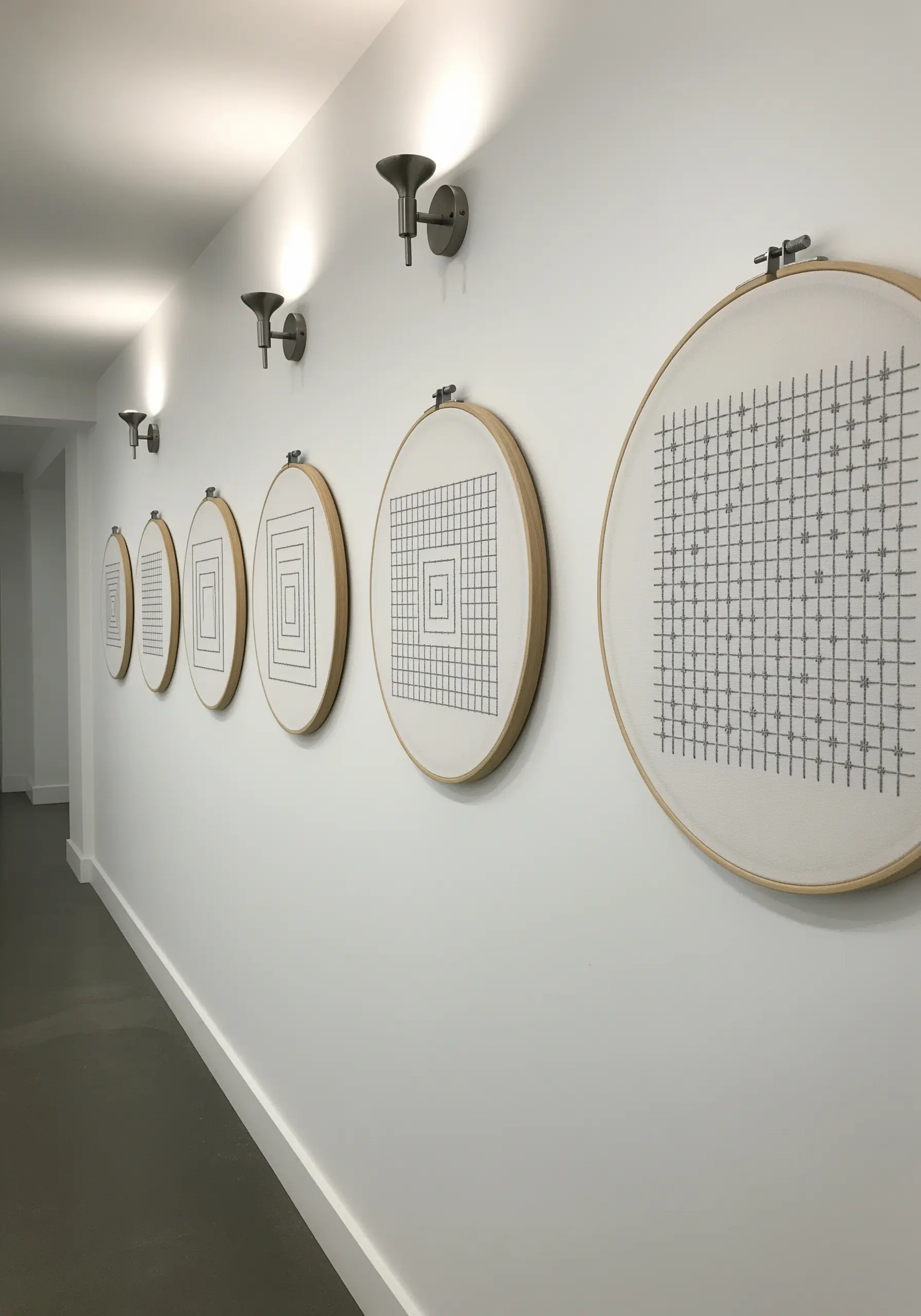 A series of embroidery hoops in a hallway showing the progression of a geometric grid pattern.