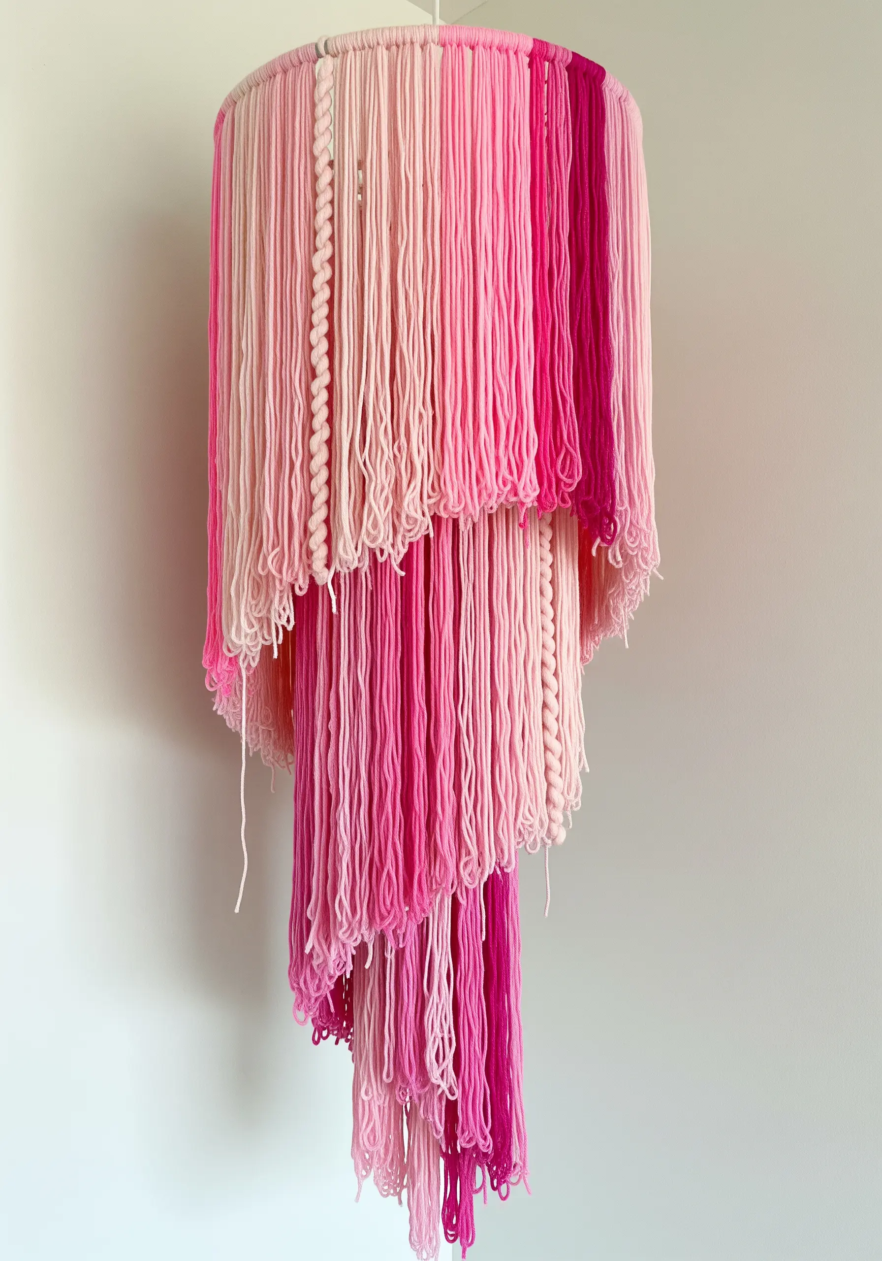 A tiered, cascading chandelier made from strands of pink yarn in various shades and textures.