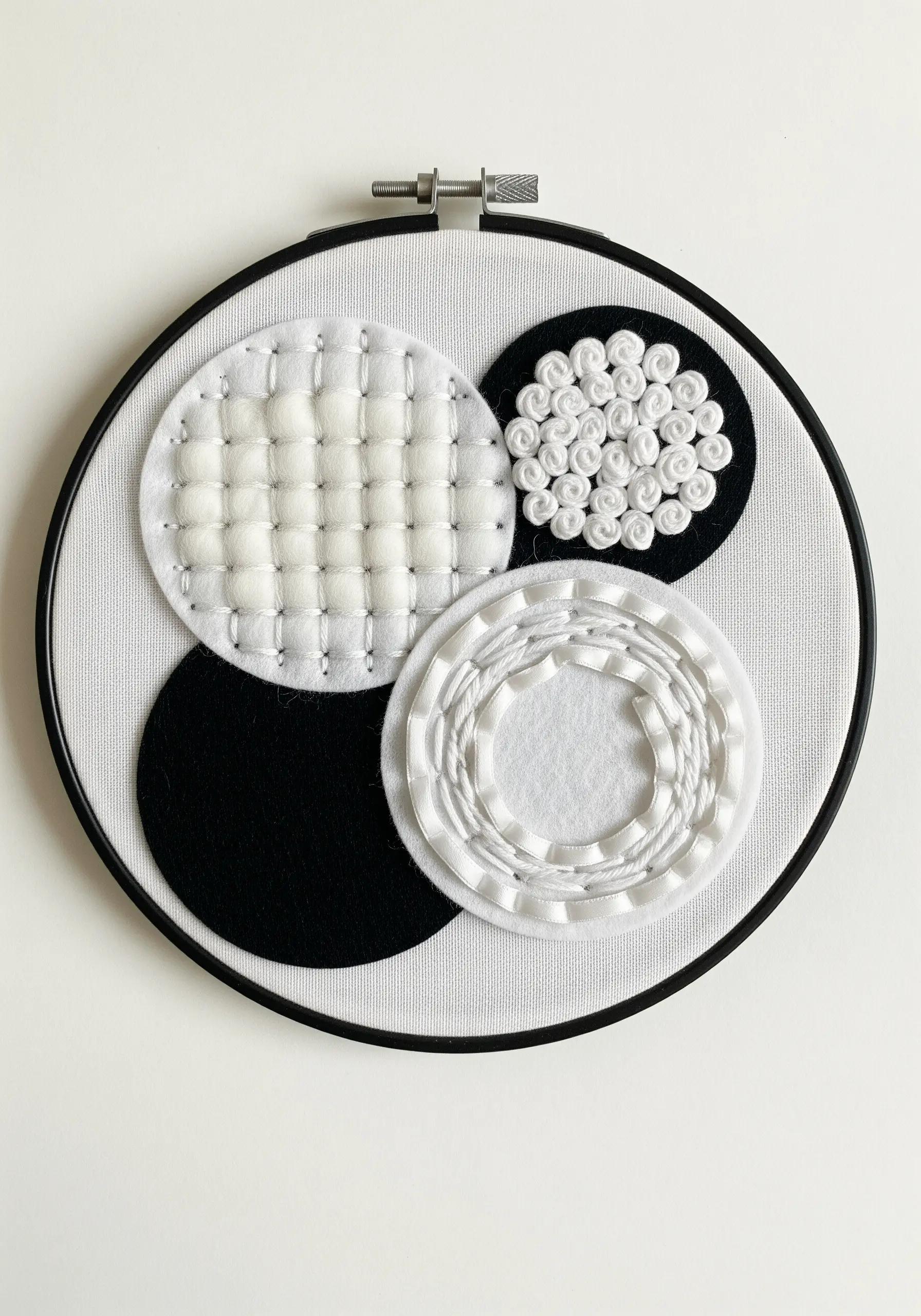 Monochrome abstract design using felt appliqué, woven ribbon, and padded stitching.