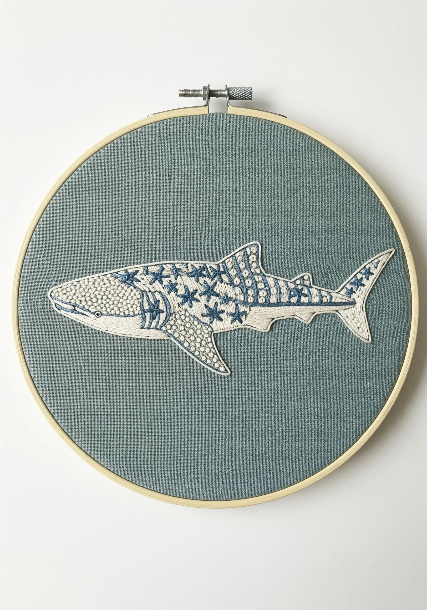A whale shark embroidery filled with various white and blue stitch patterns on gray-blue fabric.