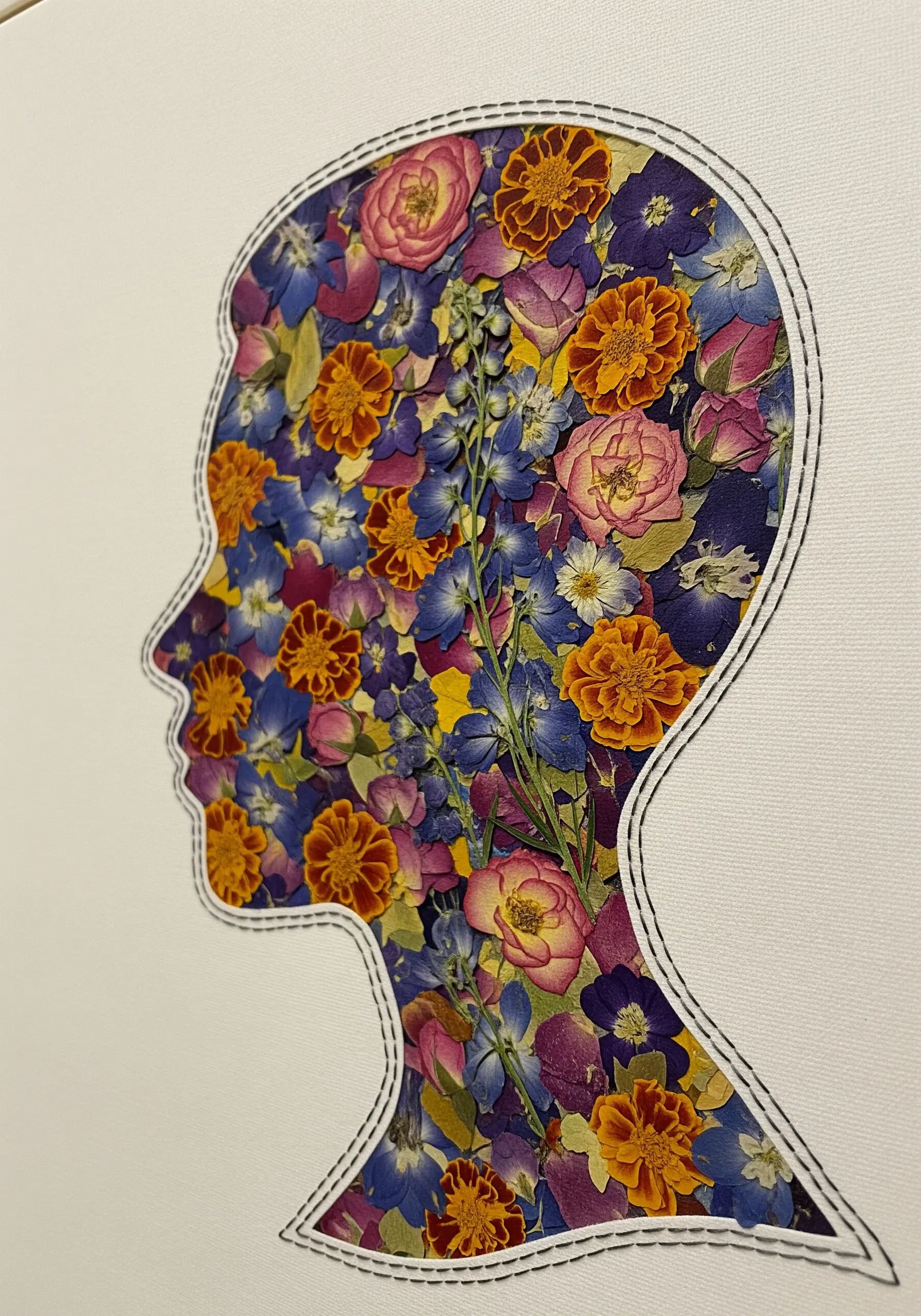 A human head silhouette outlined in black thread, filled with a dense collage of colorful pressed flowers.