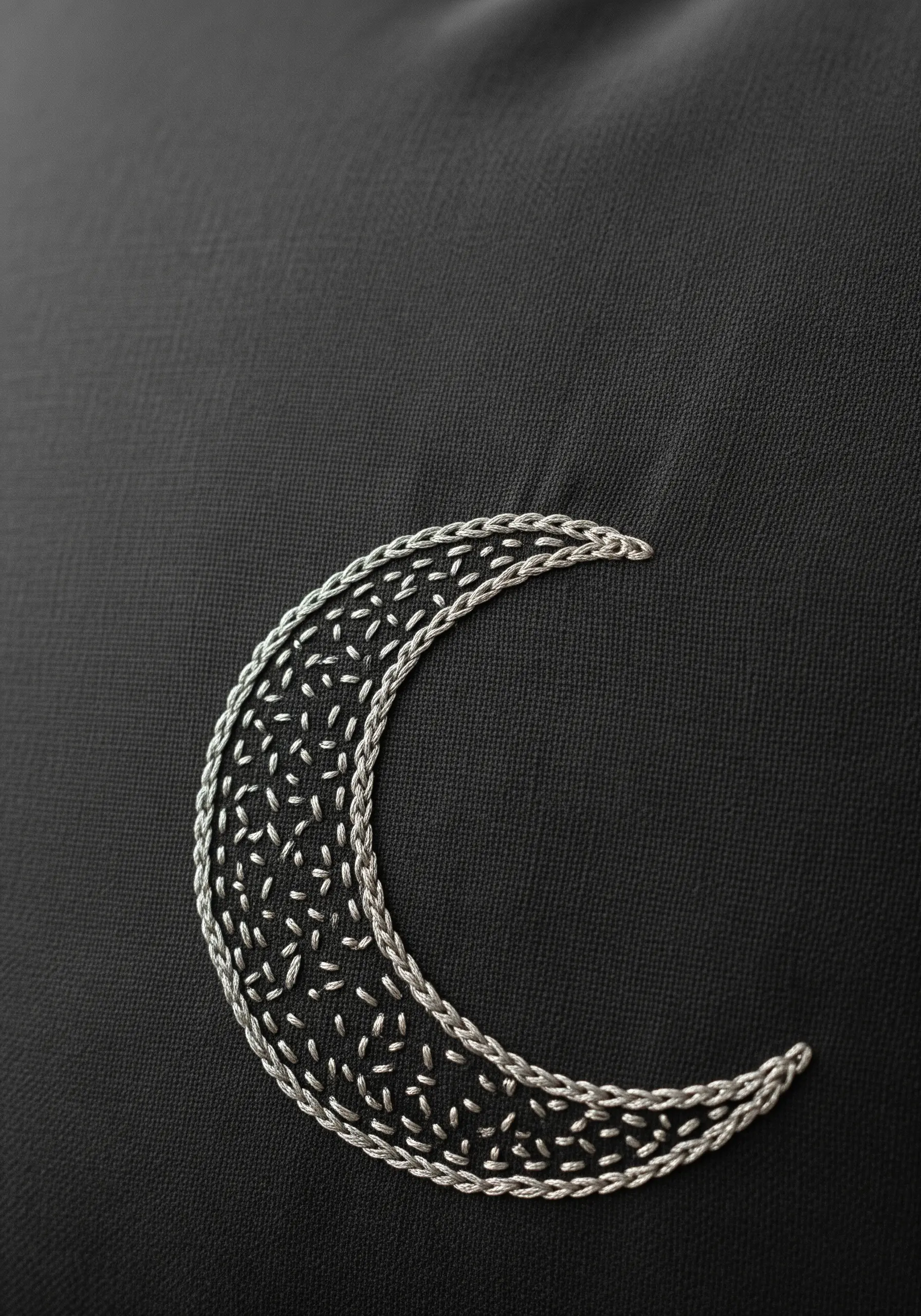 Silver crescent moon with a textured seed stitch fill on black fabric.