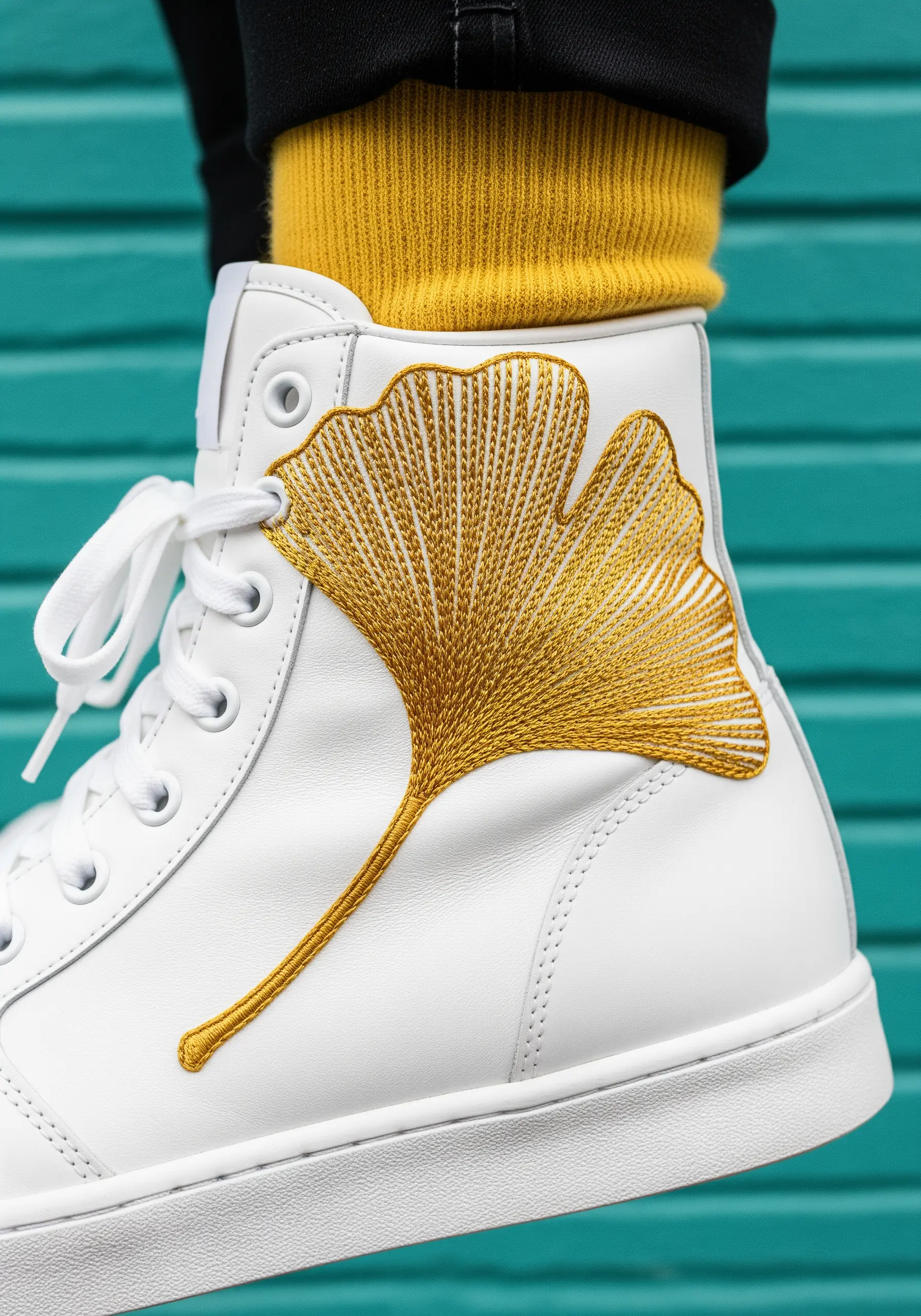 A large, golden-yellow ginkgo leaf embroidered on a white high-top leather sneaker.