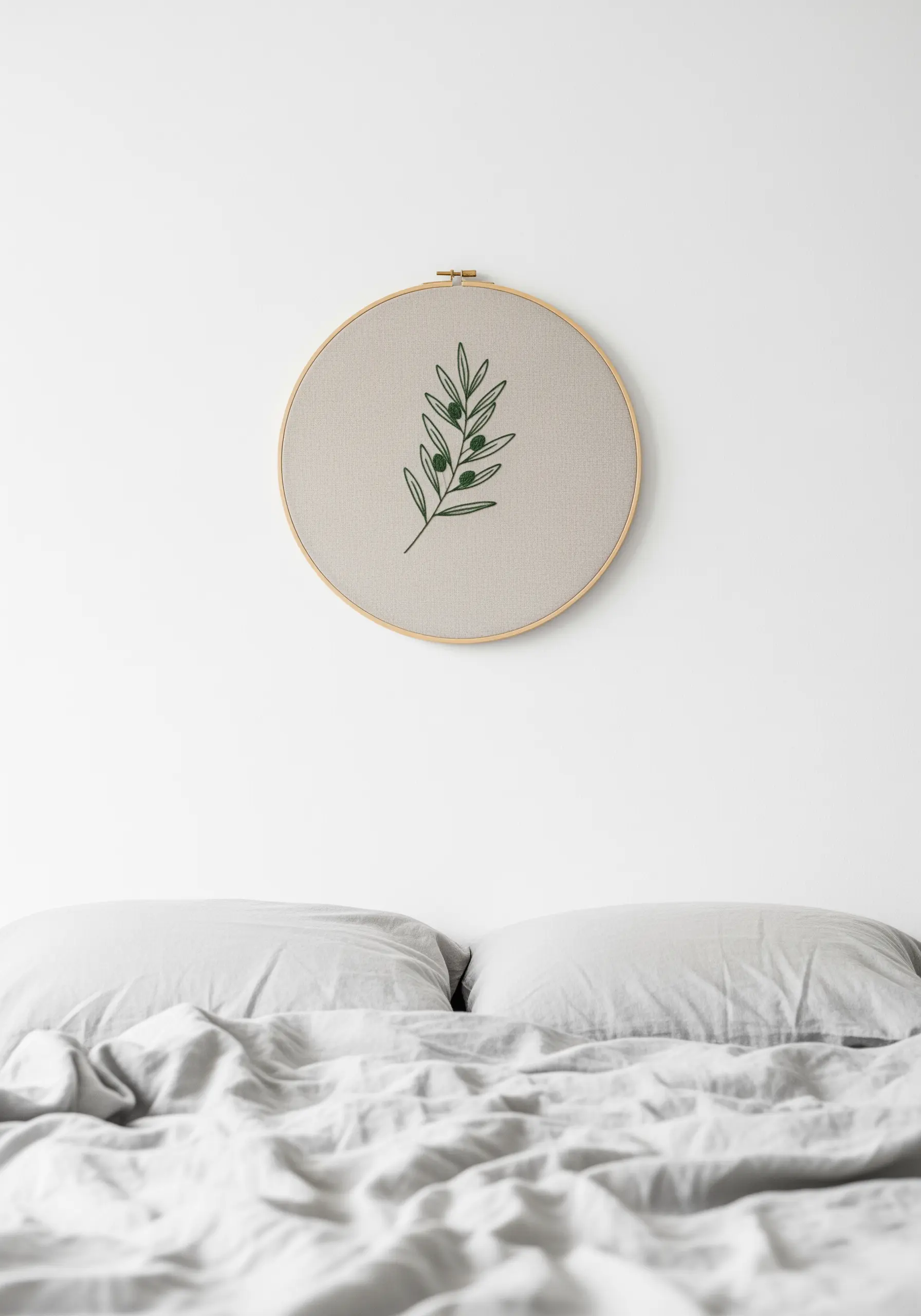 A single embroidery hoop with an olive branch motif hanging on a white wall