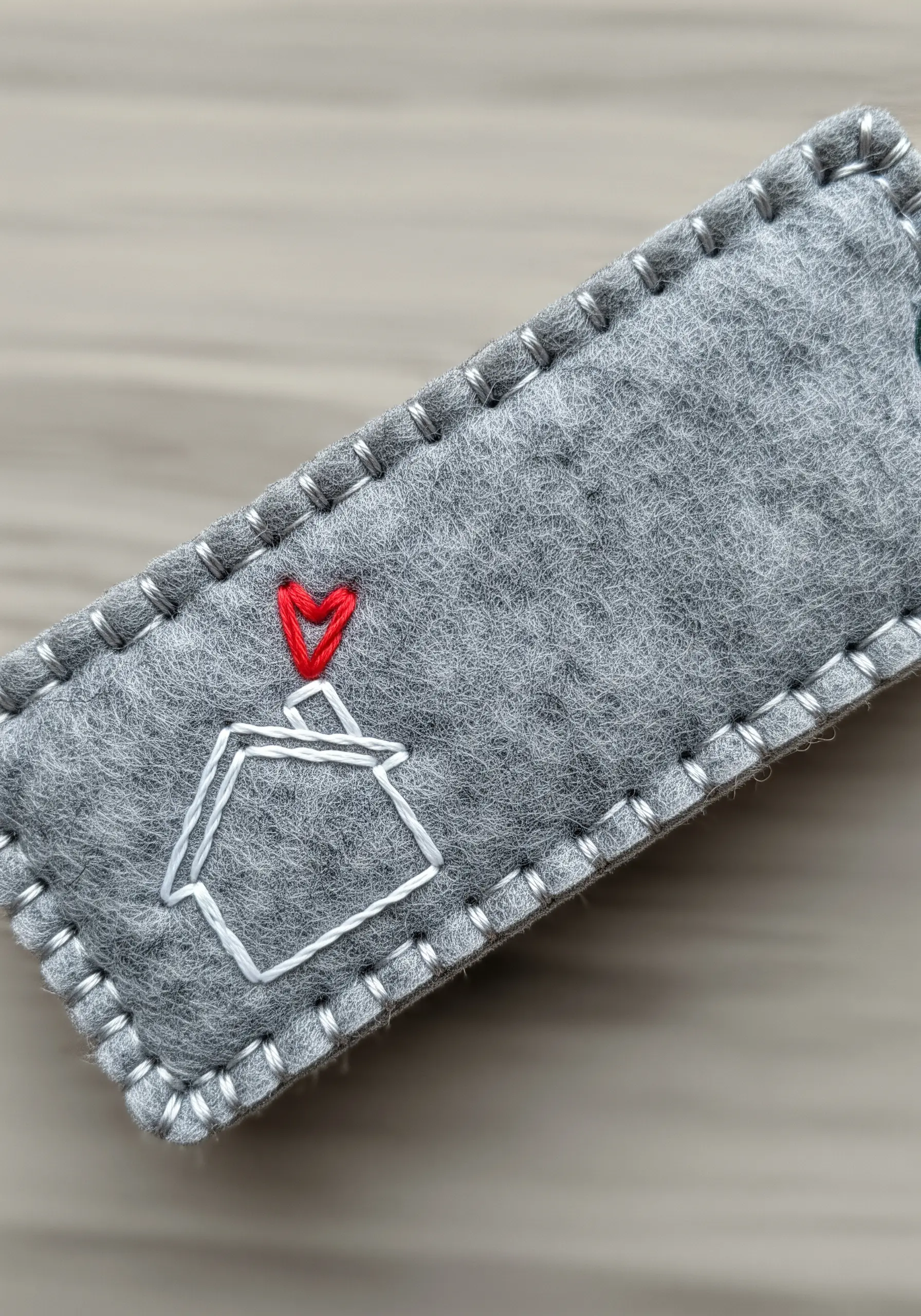 A grey felt keychain with a simple house motif, neatly finished with a white blanket stitch edge.