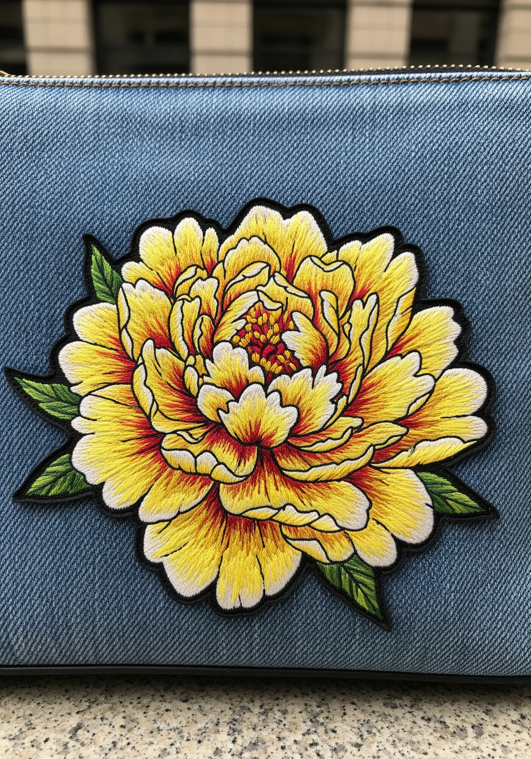 A yellow peony patch with a thick, clean satin stitch border on a denim bag.