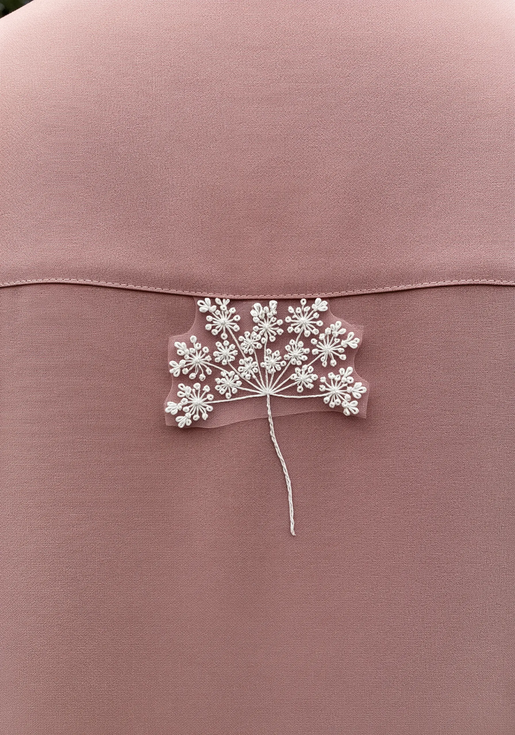 A delicate embroidery of Queen Anne's Lace on a sheer patch, stitched onto a dusty pink fabric.