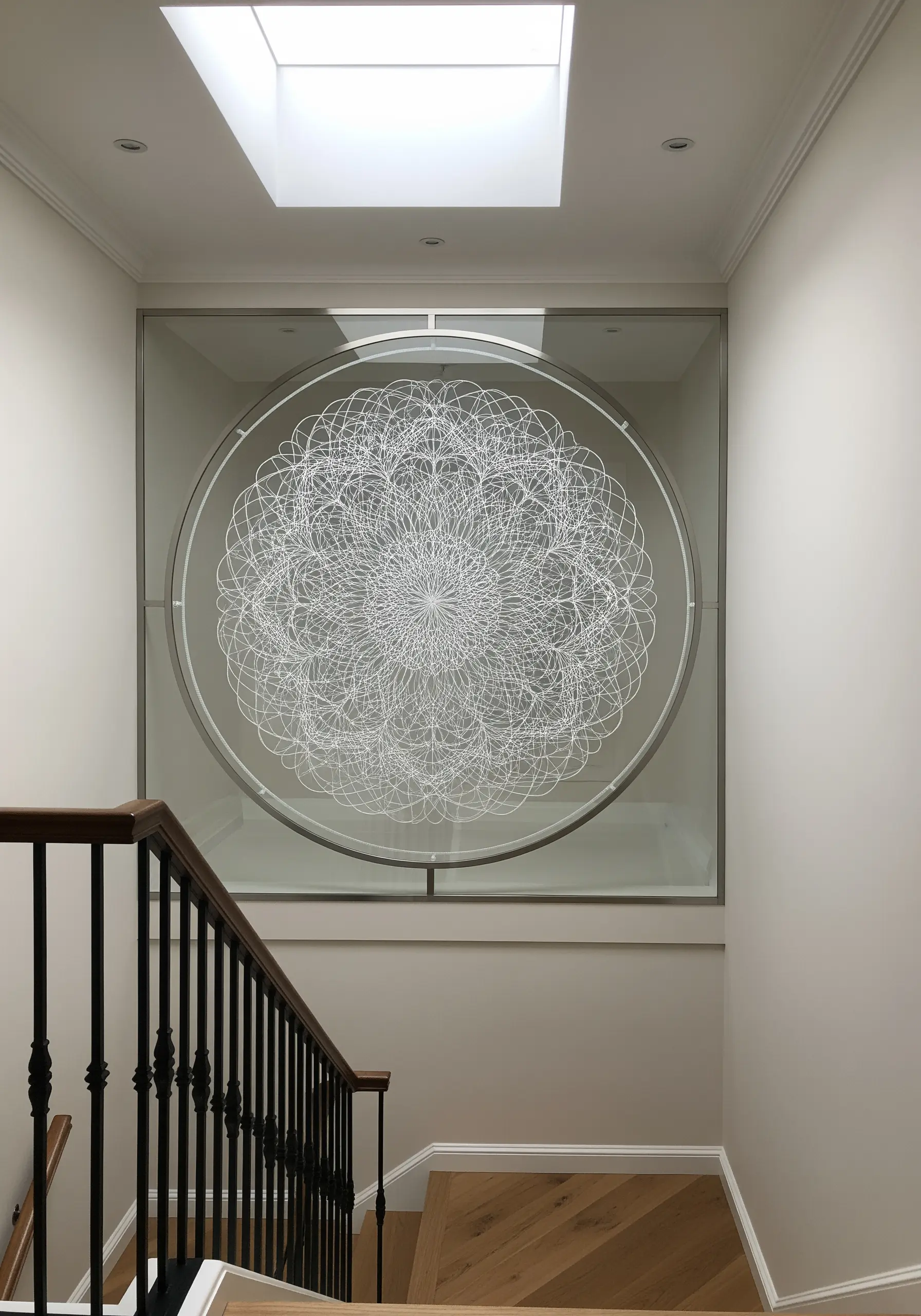 An intricate white thread mandala embroidered on sheer fabric, framed between glass.