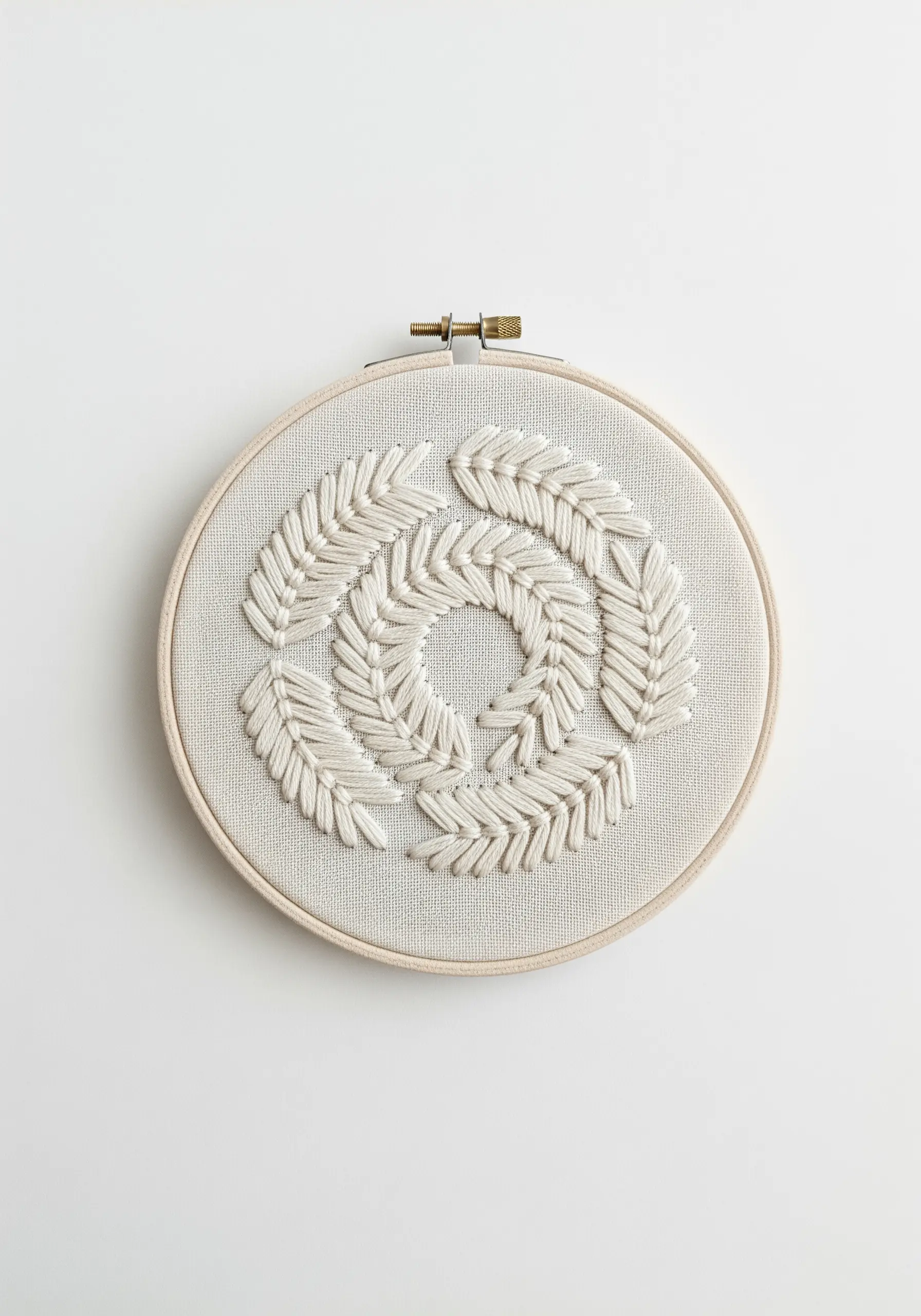 A circular wreath motif embroidered in white thread using overlapping, directional fishbone stitches.