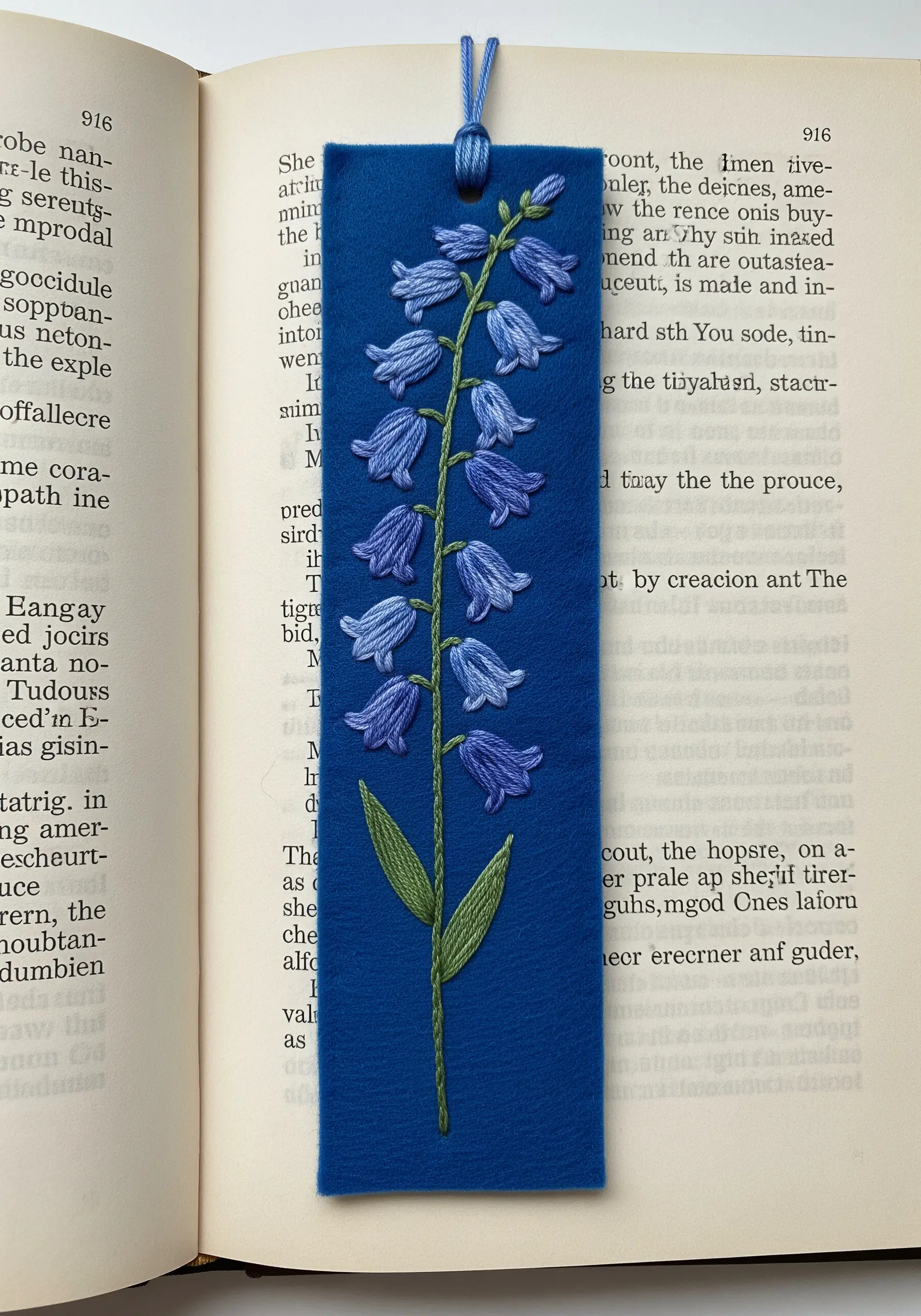 A single stalk of bluebell flowers with green leaves embroidered onto a blue felt bookmark.