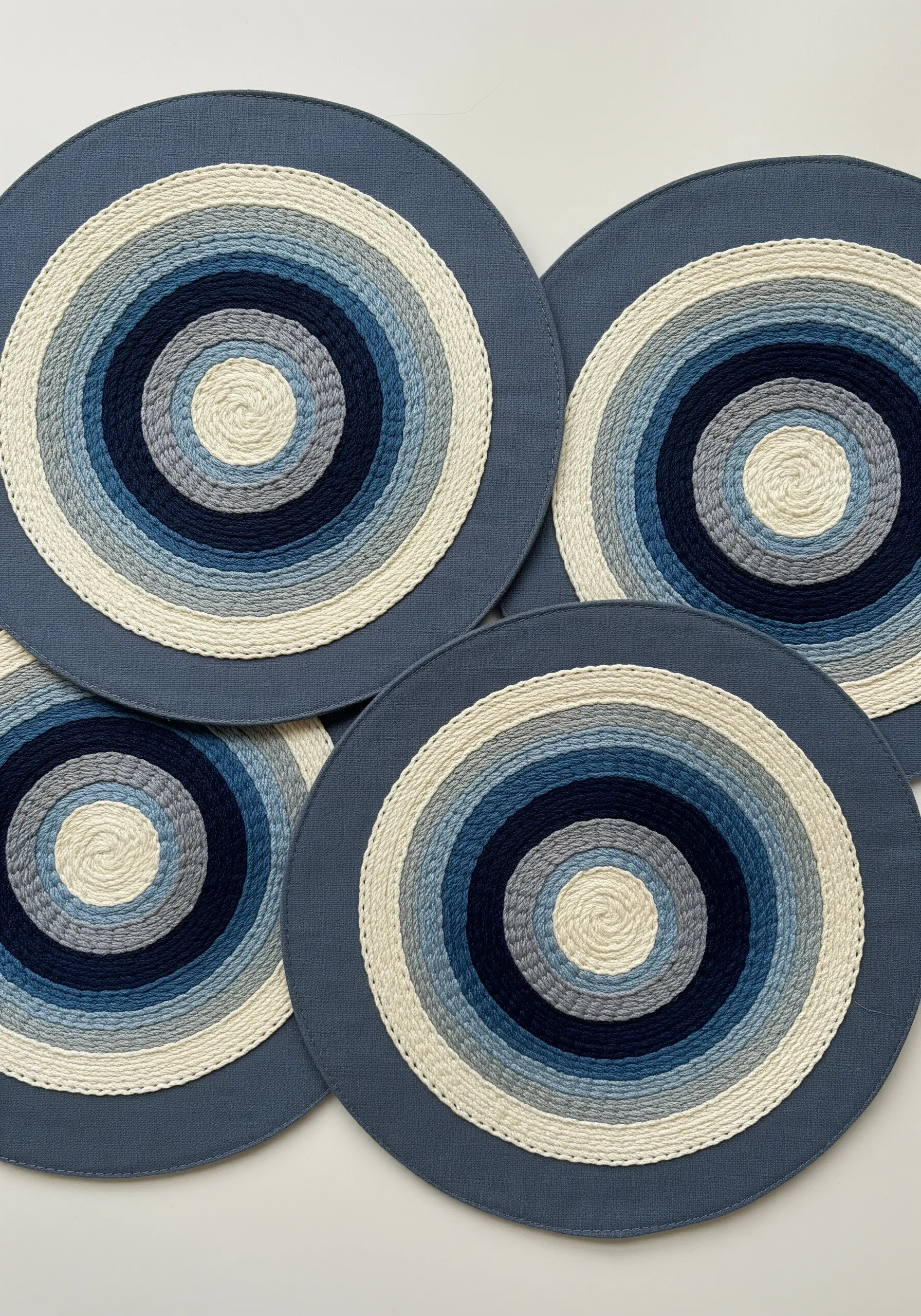 Four circular placemats with concentric rings of couched rope in shades of blue and white.