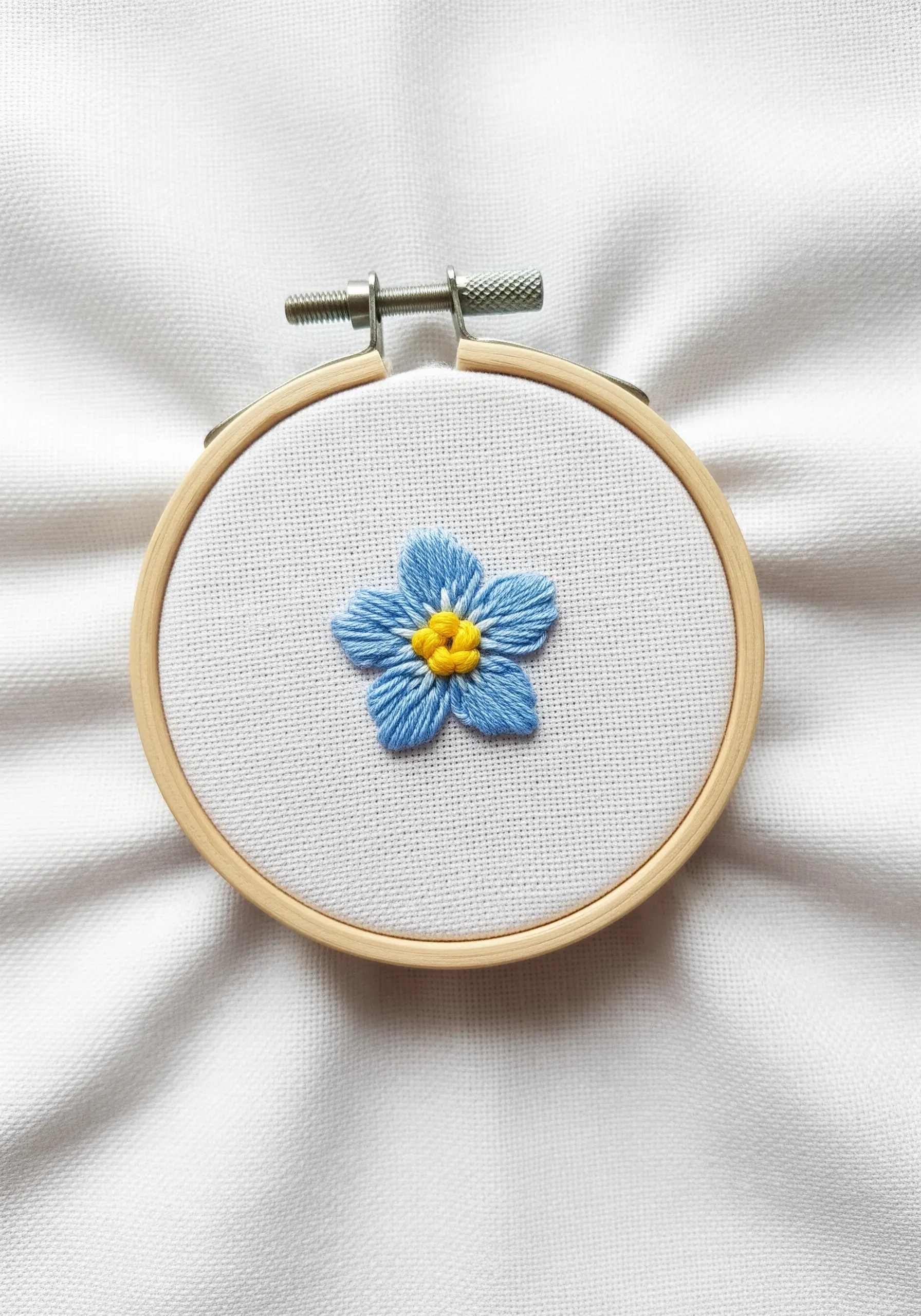 A simple blue forget-me-not flower with a yellow center, stitched with lazy daisy stitches.