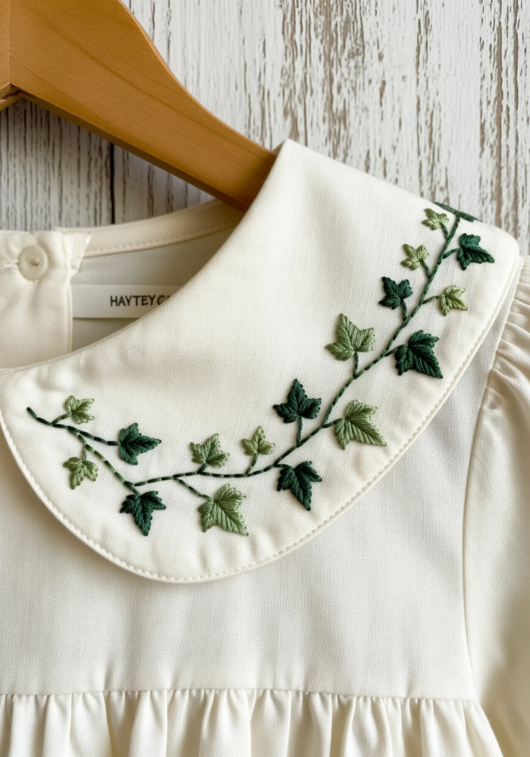 Ivy vine embroidered in shades of green on the white collar of a dress.