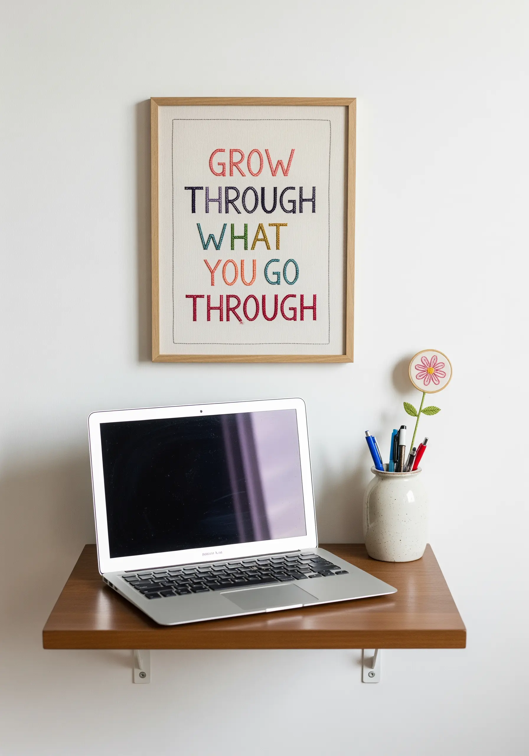 A framed embroidery piece with the quote 'Grow through what you go through' in colorful backstitch.