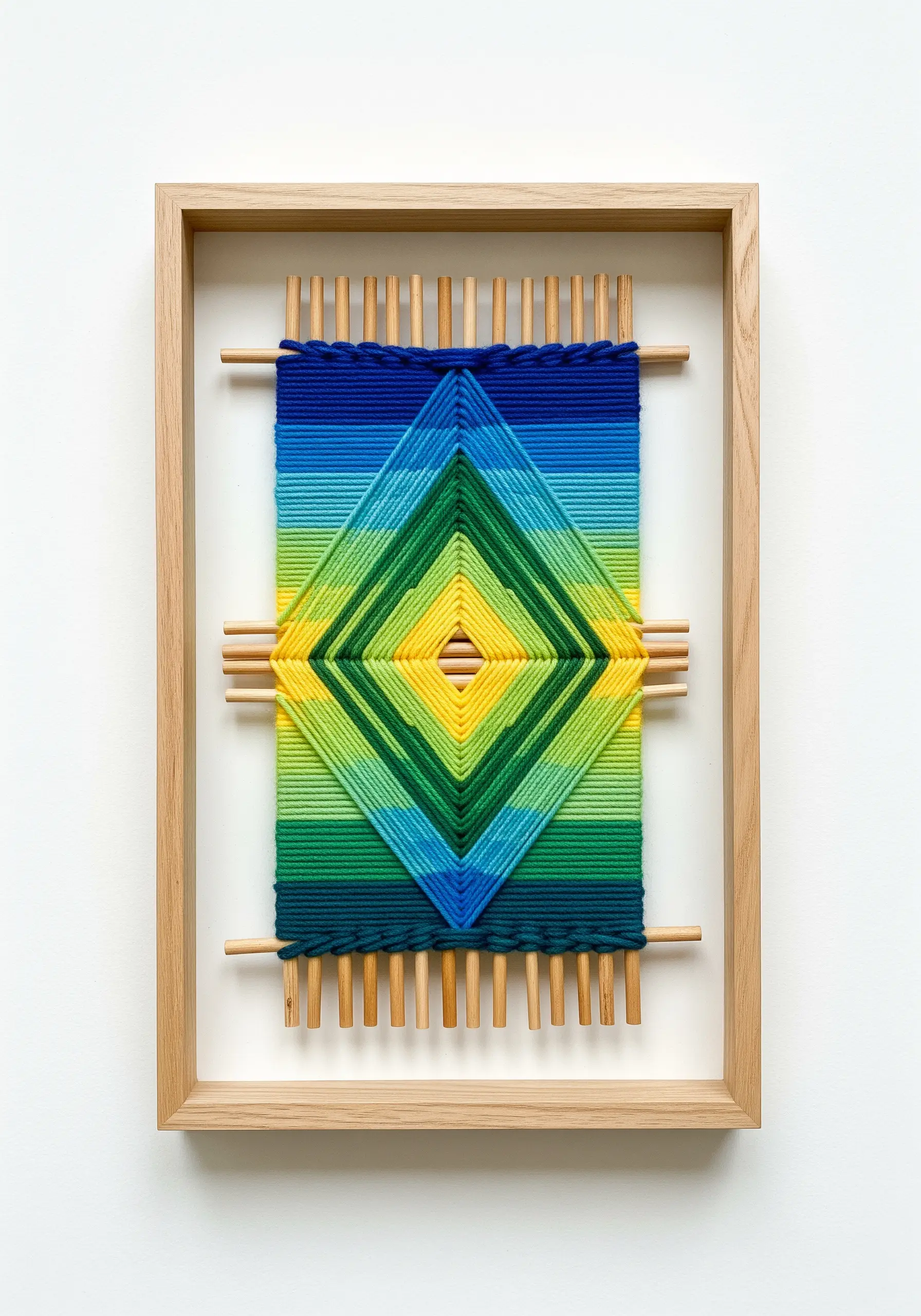 A framed God's Eye weaving with a blue, green, and yellow gradient yarn pattern.
