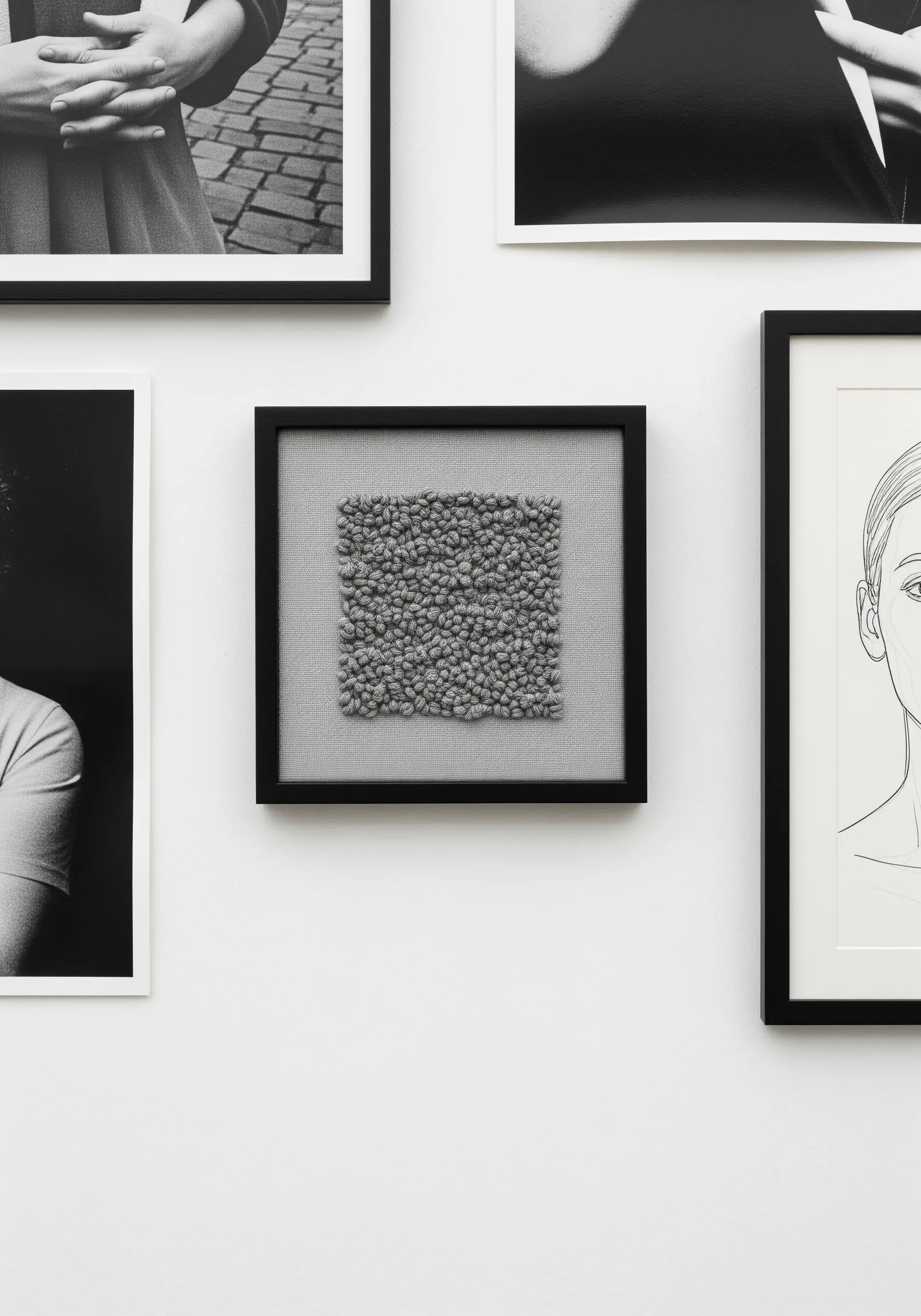 A small, framed piece of grey textured embroidery, hung on a gallery wall.