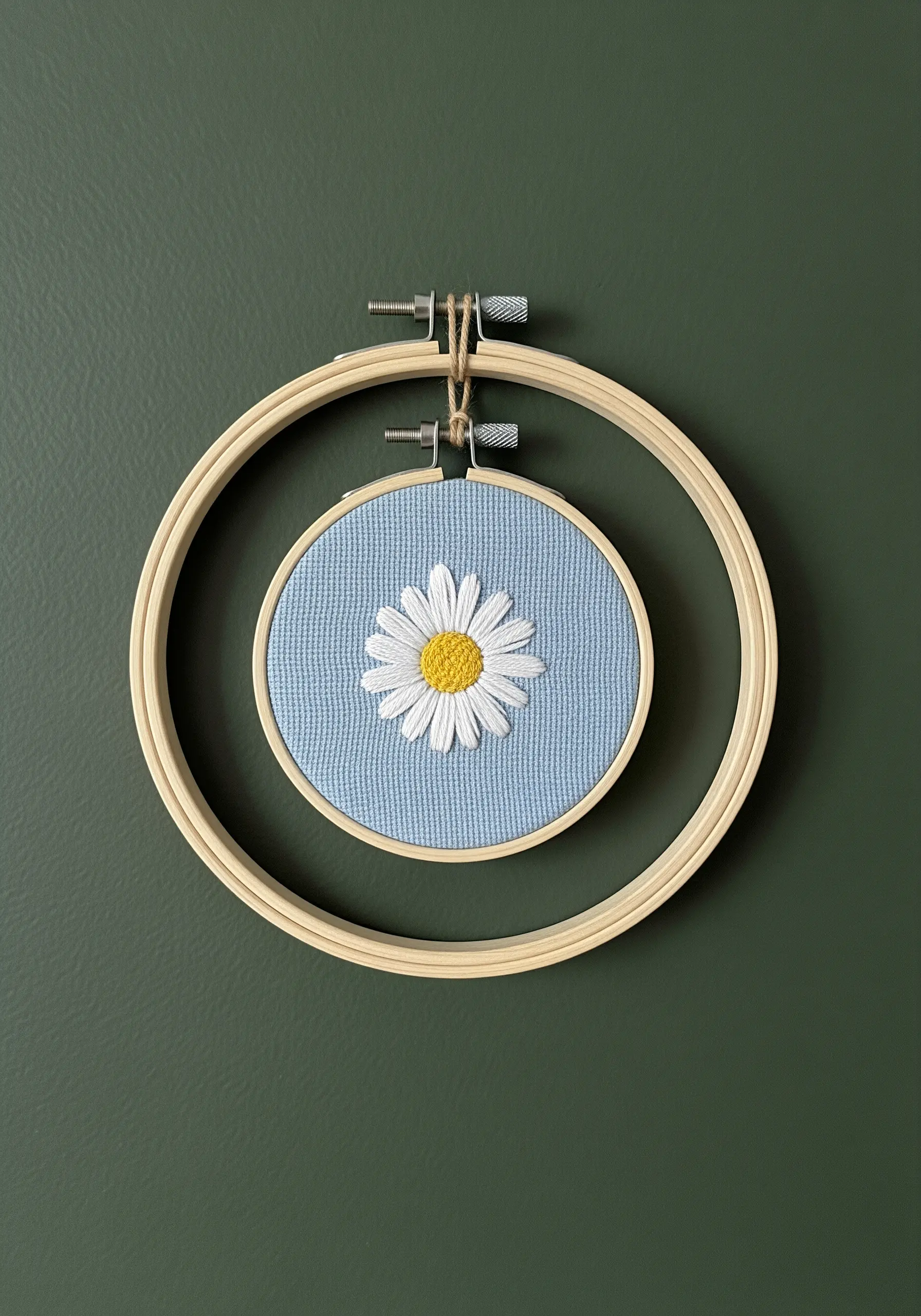 An embroidered daisy in a small hoop, framed within a larger empty hoop.