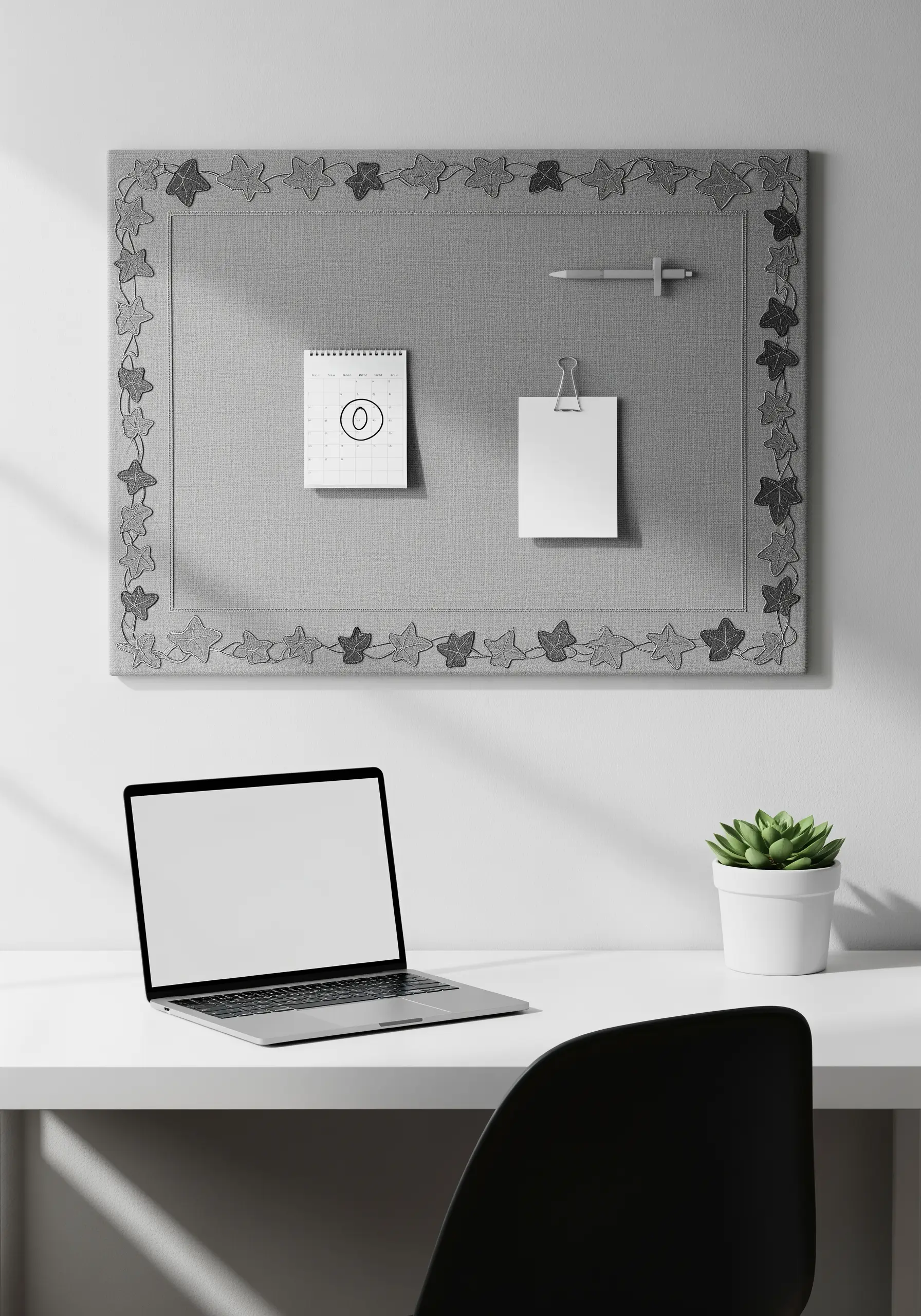 A grey fabric pinboard framed with a simple, tone-on-tone embroidered leaf border.