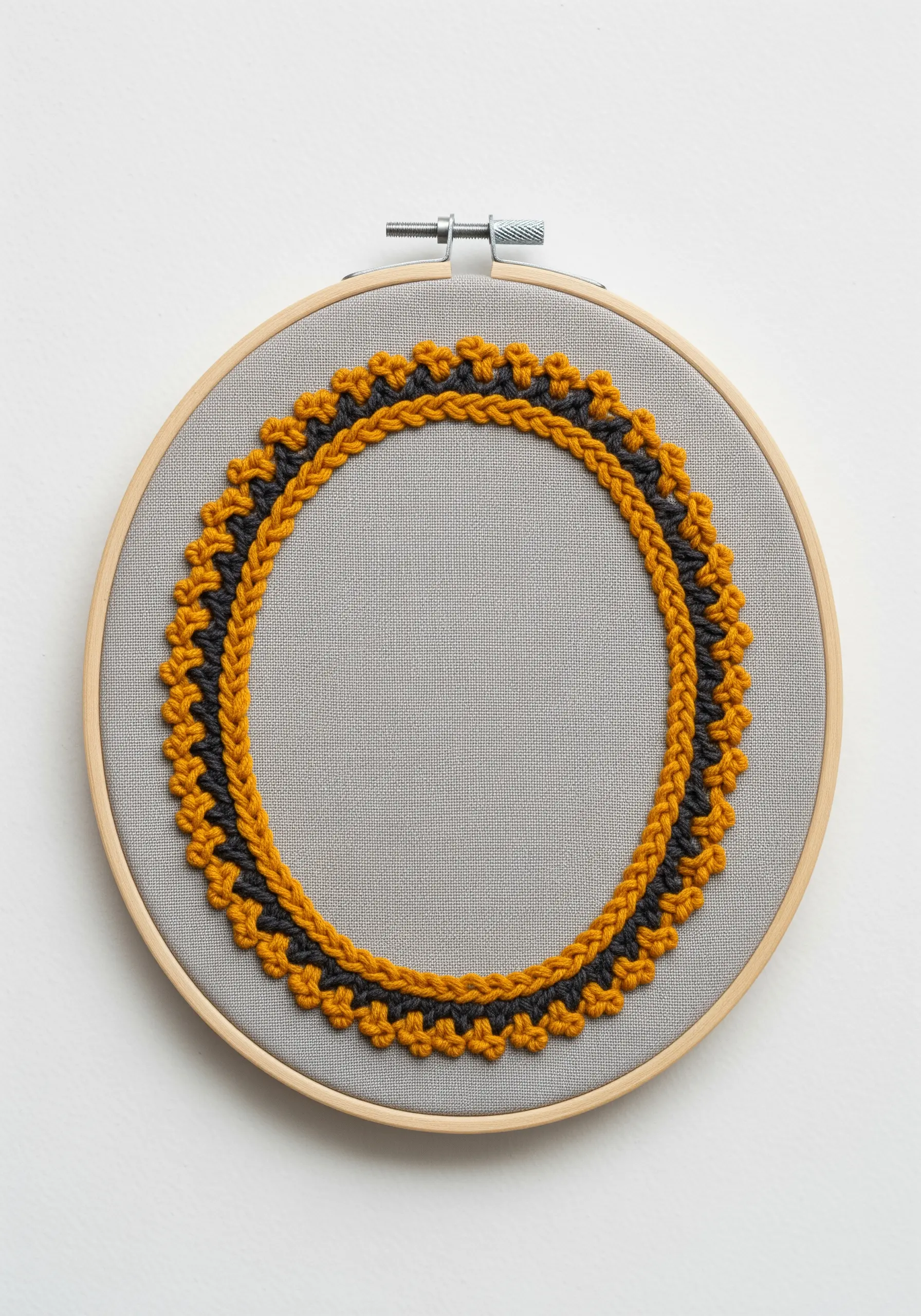 Embroidery hoop with a textured, two-color geometric border in yellow and grey on neutral fabric.