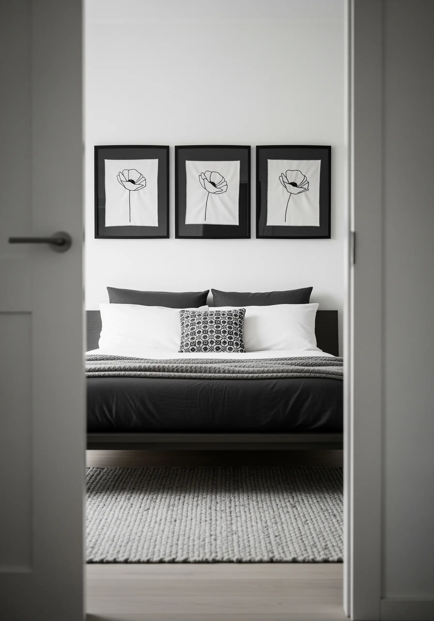 Three black-framed minimalist line art embroideries of poppies hanging above a bed.