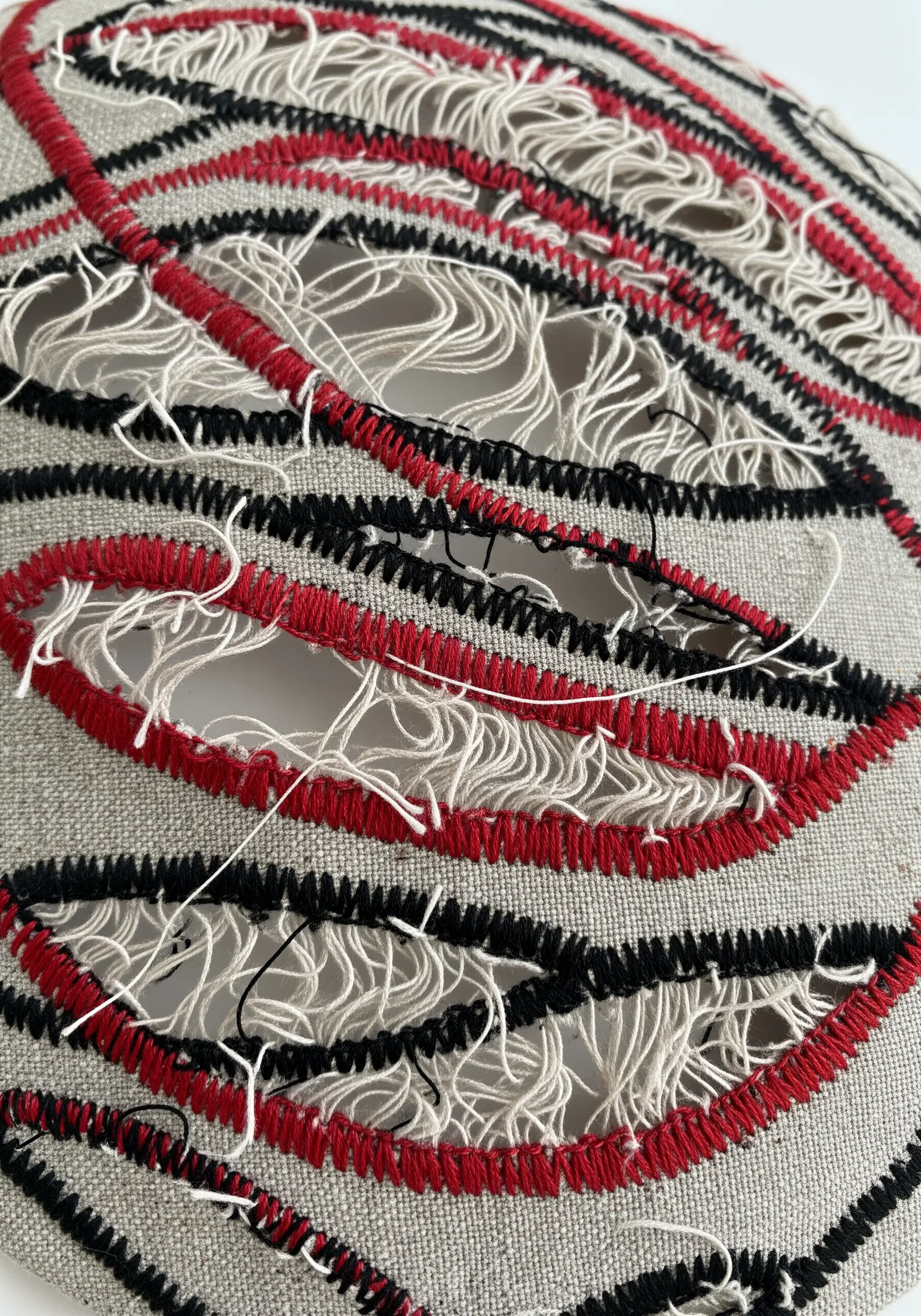Fabric with cut-out sections bordered by red and black satin stitch.