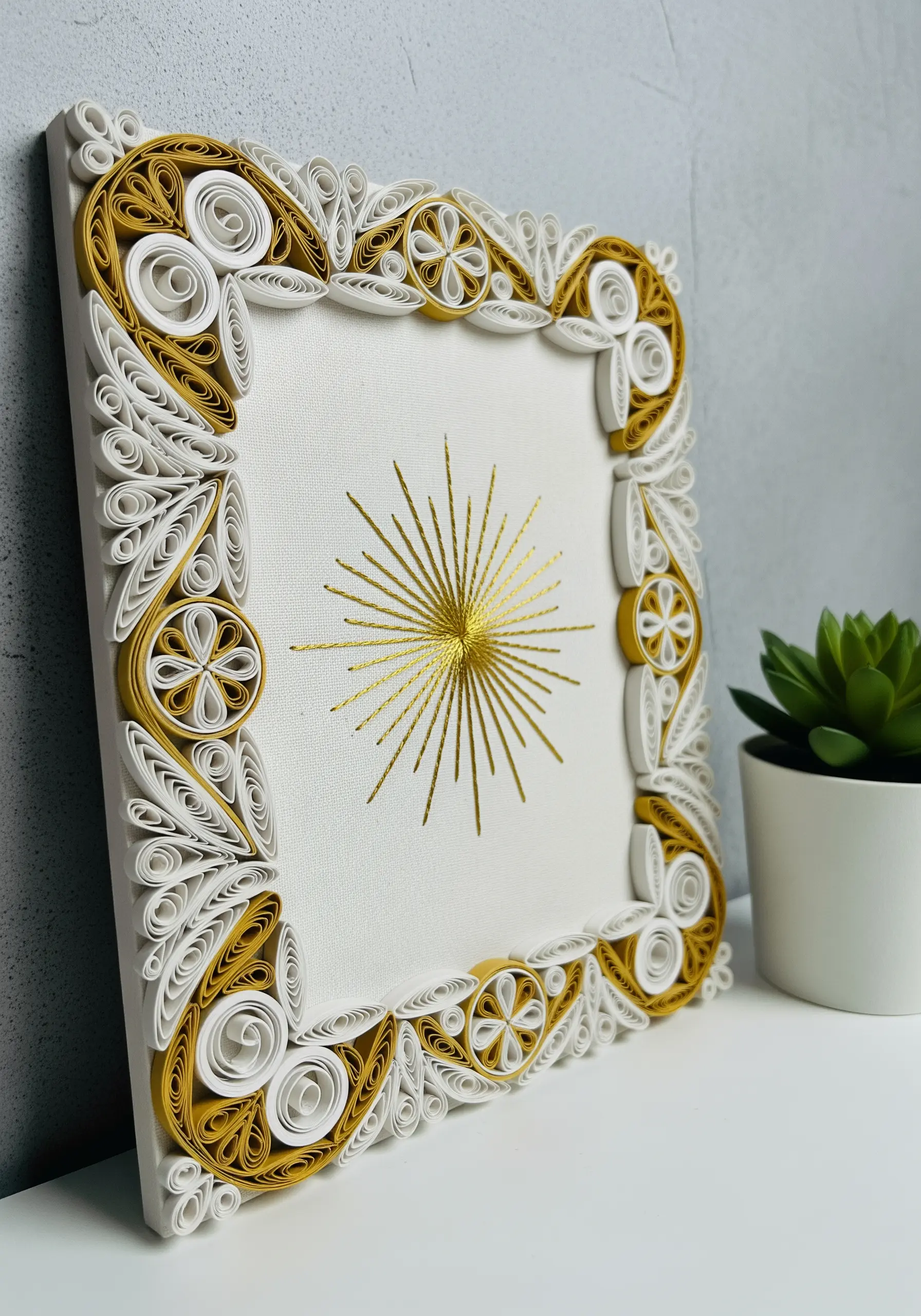 Minimal gold sunburst embroidery framed with intricate white and gold paper quilling.
