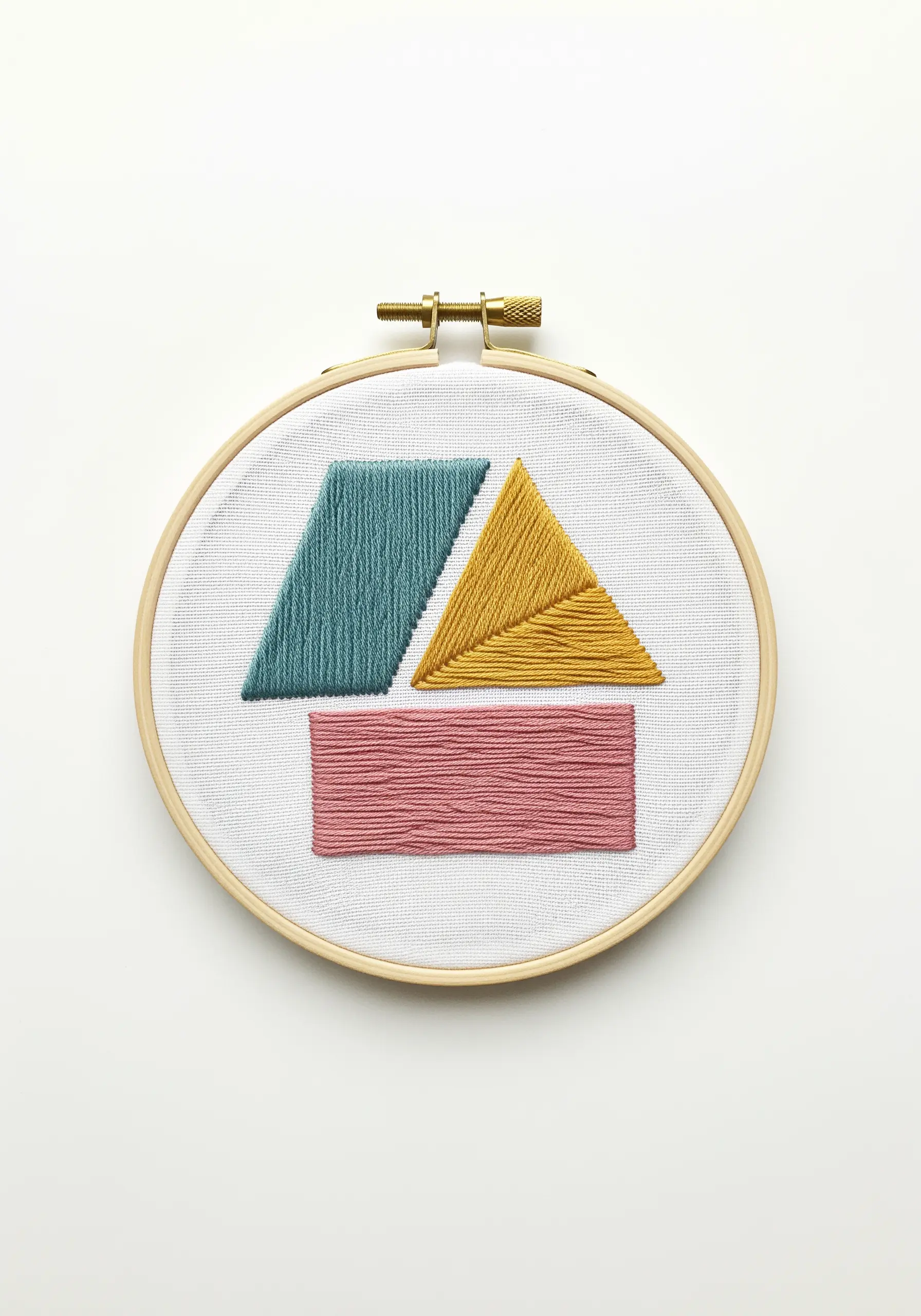 Three abstract geometric shapes filled with satin stitch in teal, yellow, and pink.