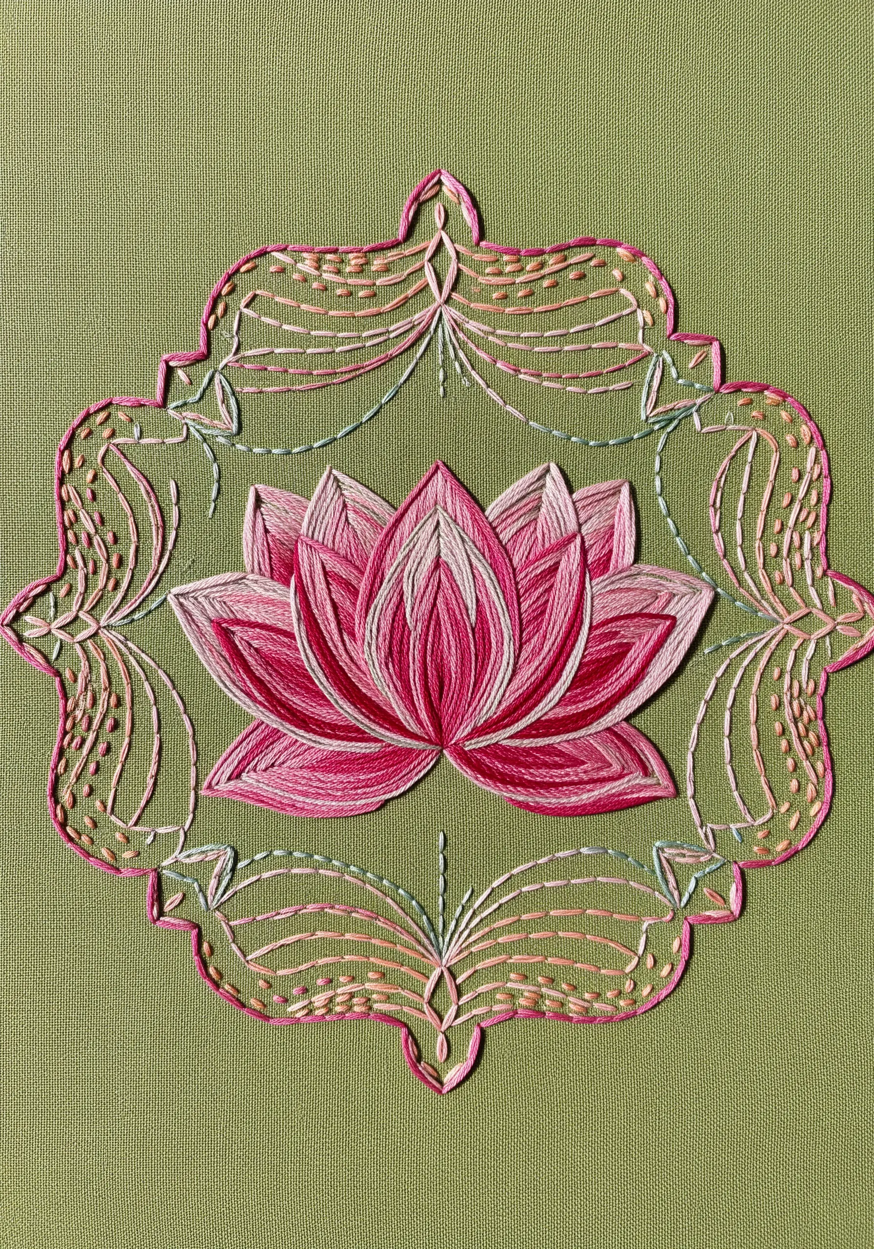 A pink lotus flower embroidered in satin stitch, enclosed in a decorative openwork frame.