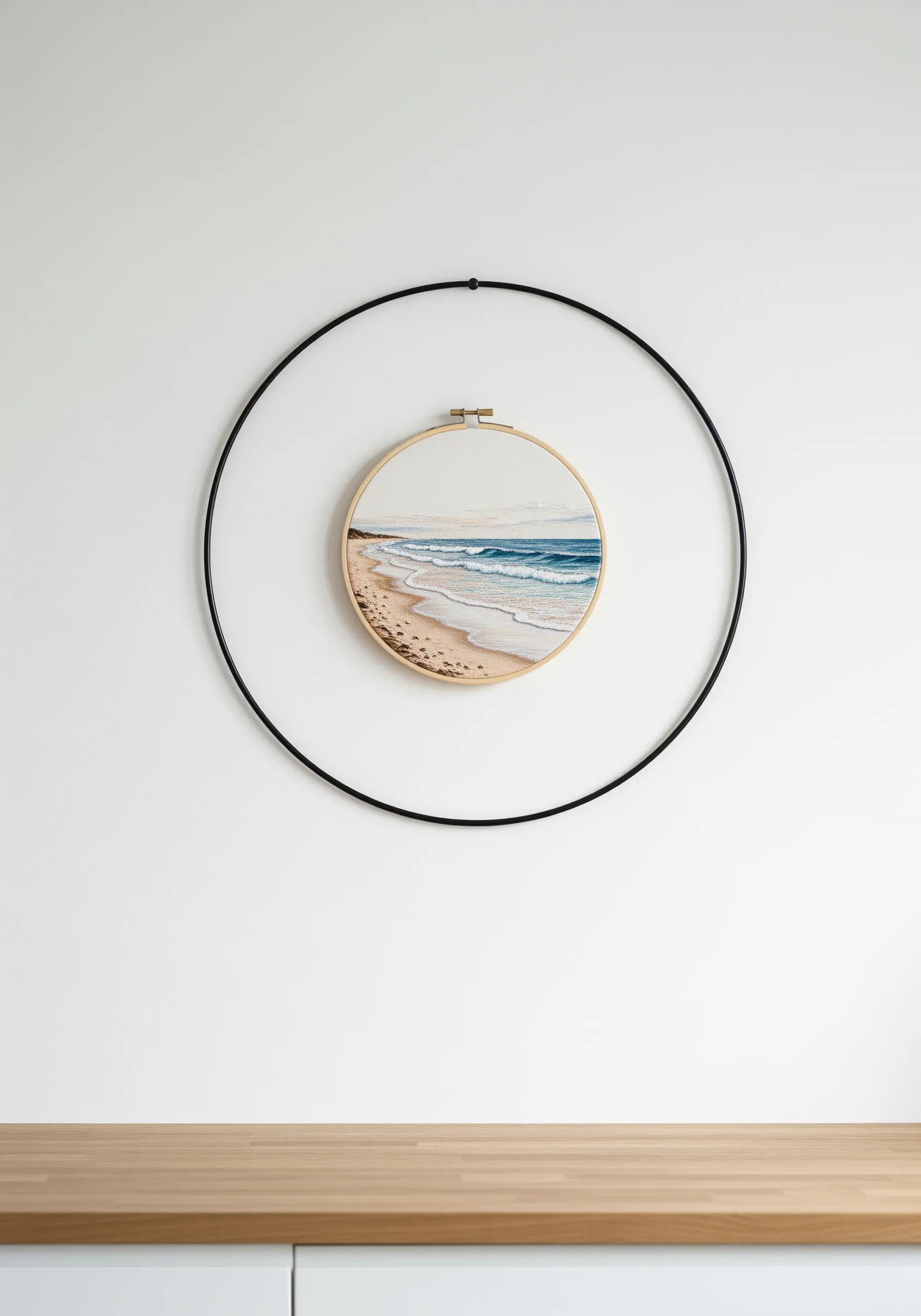 An embroidered beach scene in a wooden hoop, framed by a larger, thin black metal ring.
