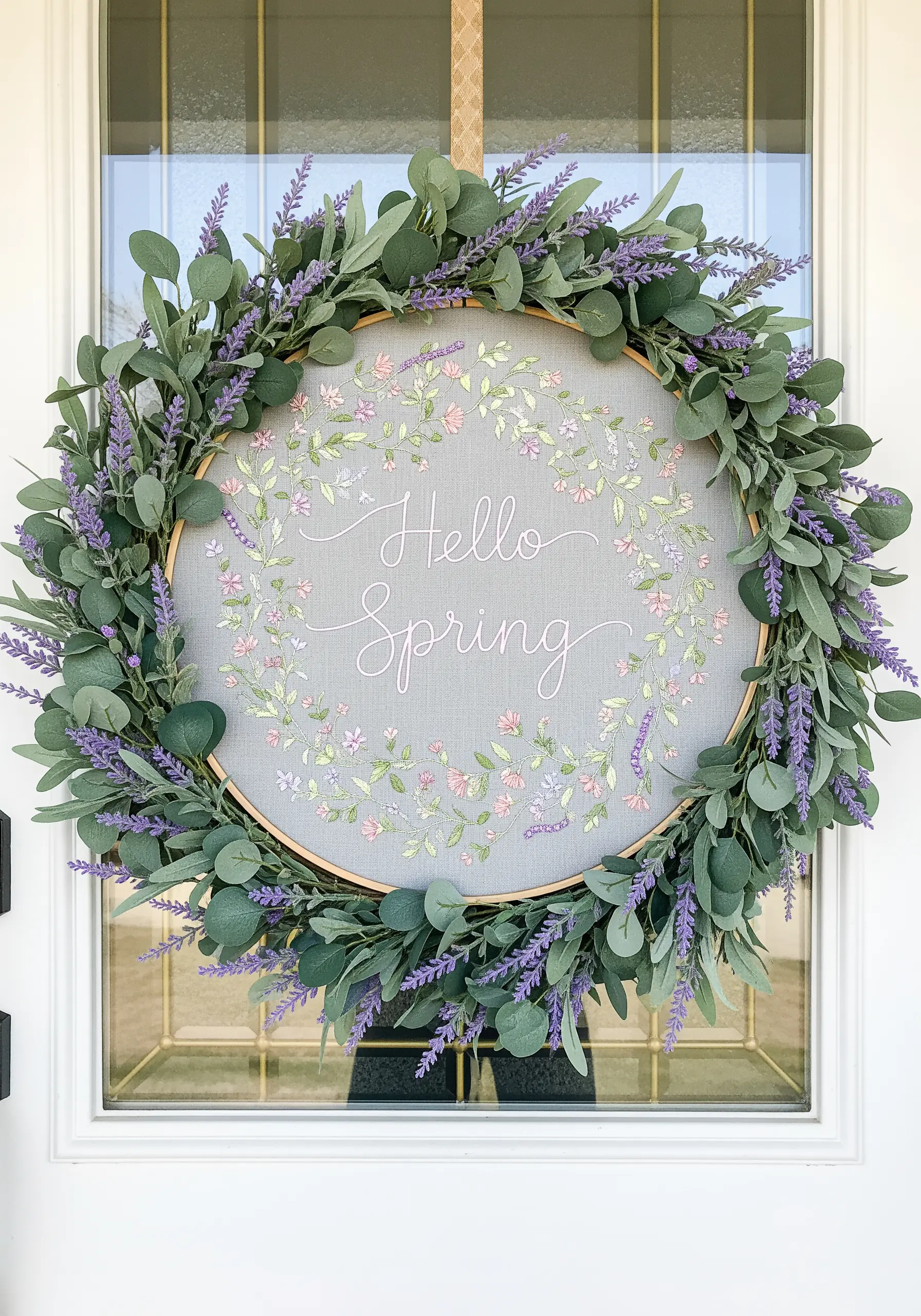 A 'Hello Spring' embroidery hoop framed with a wreath of faux eucalyptus and lavender.