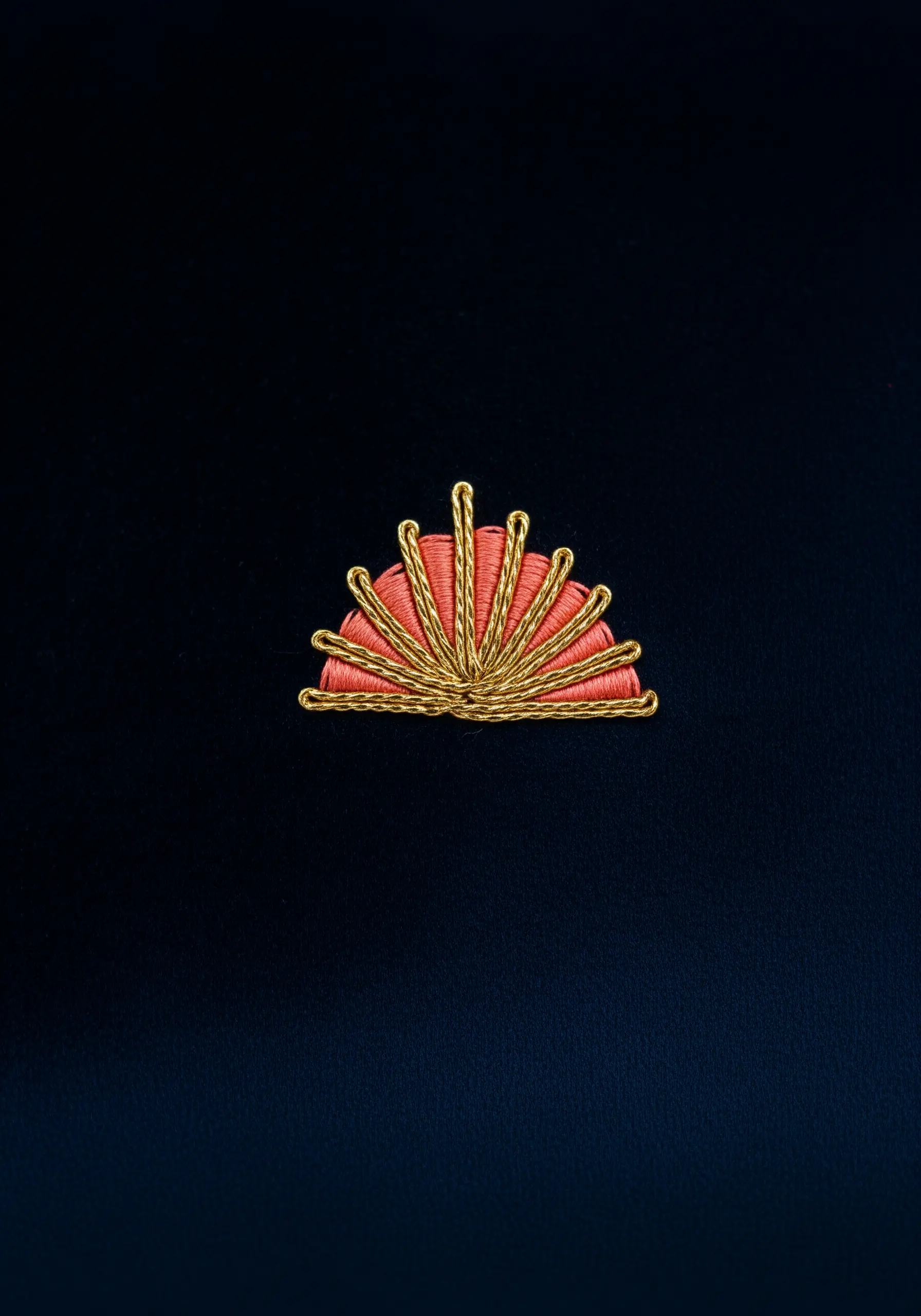 An art deco fan motif in coral satin stitch, sharply outlined with gold metallic thread.