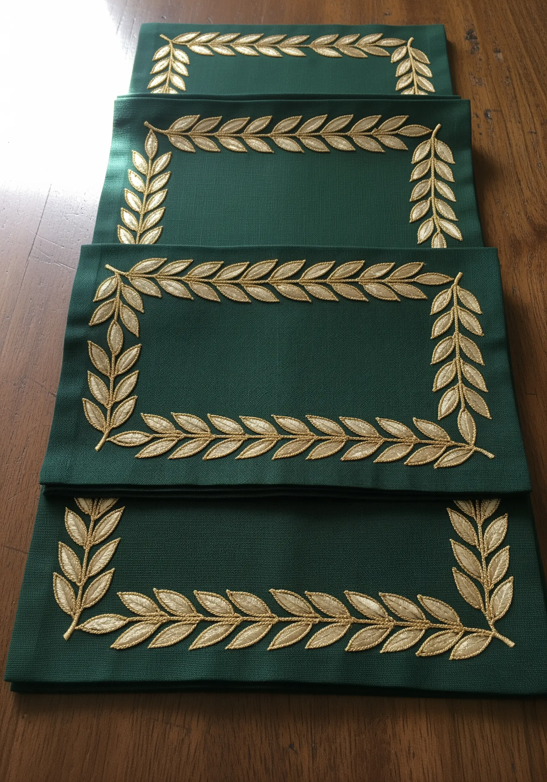 Dark green placemats framed with a border of laurel leaves embroidered in gold metallic thread.
