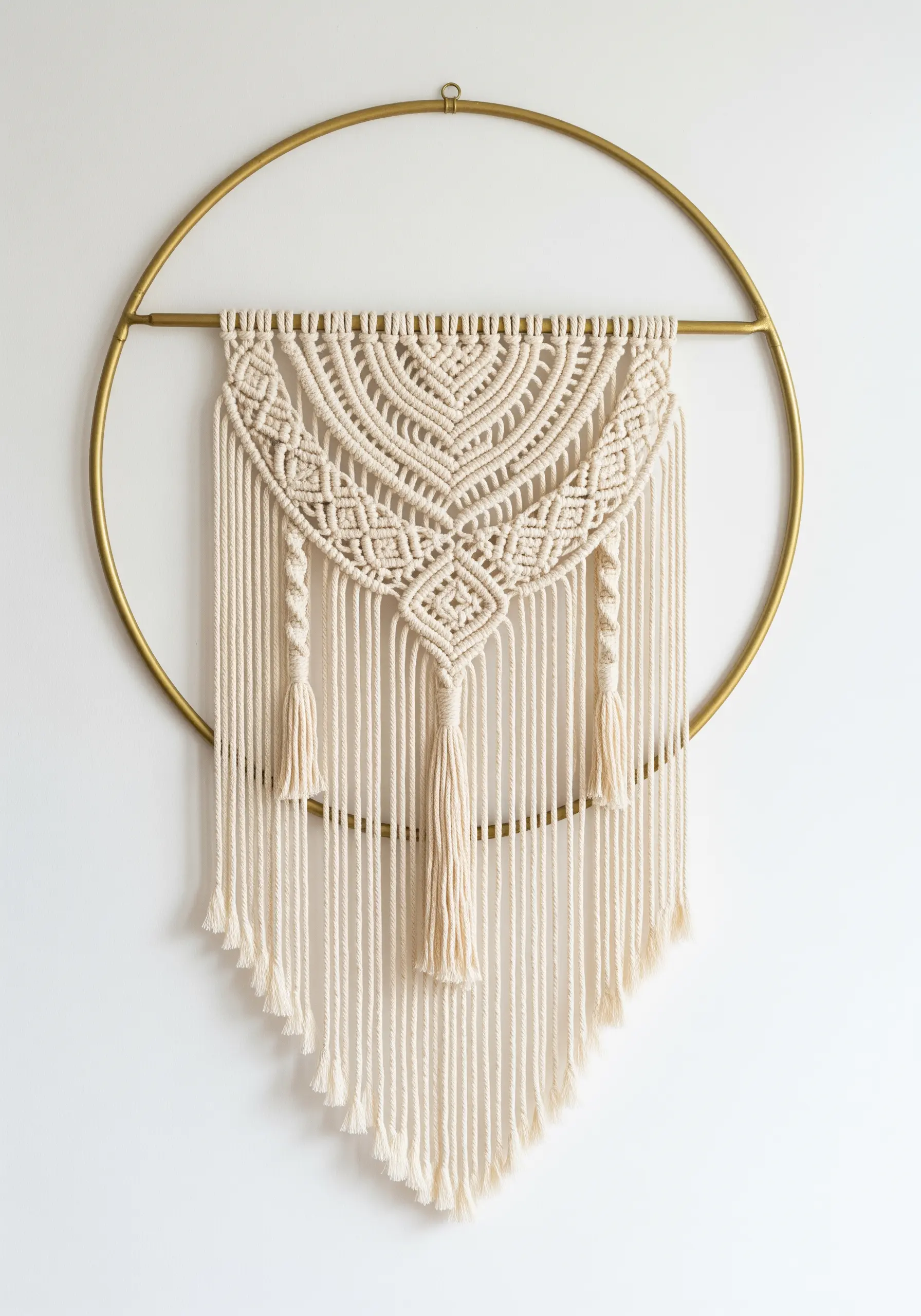 An intricate macrame design hanging from the center of a large, minimalist gold metal hoop.