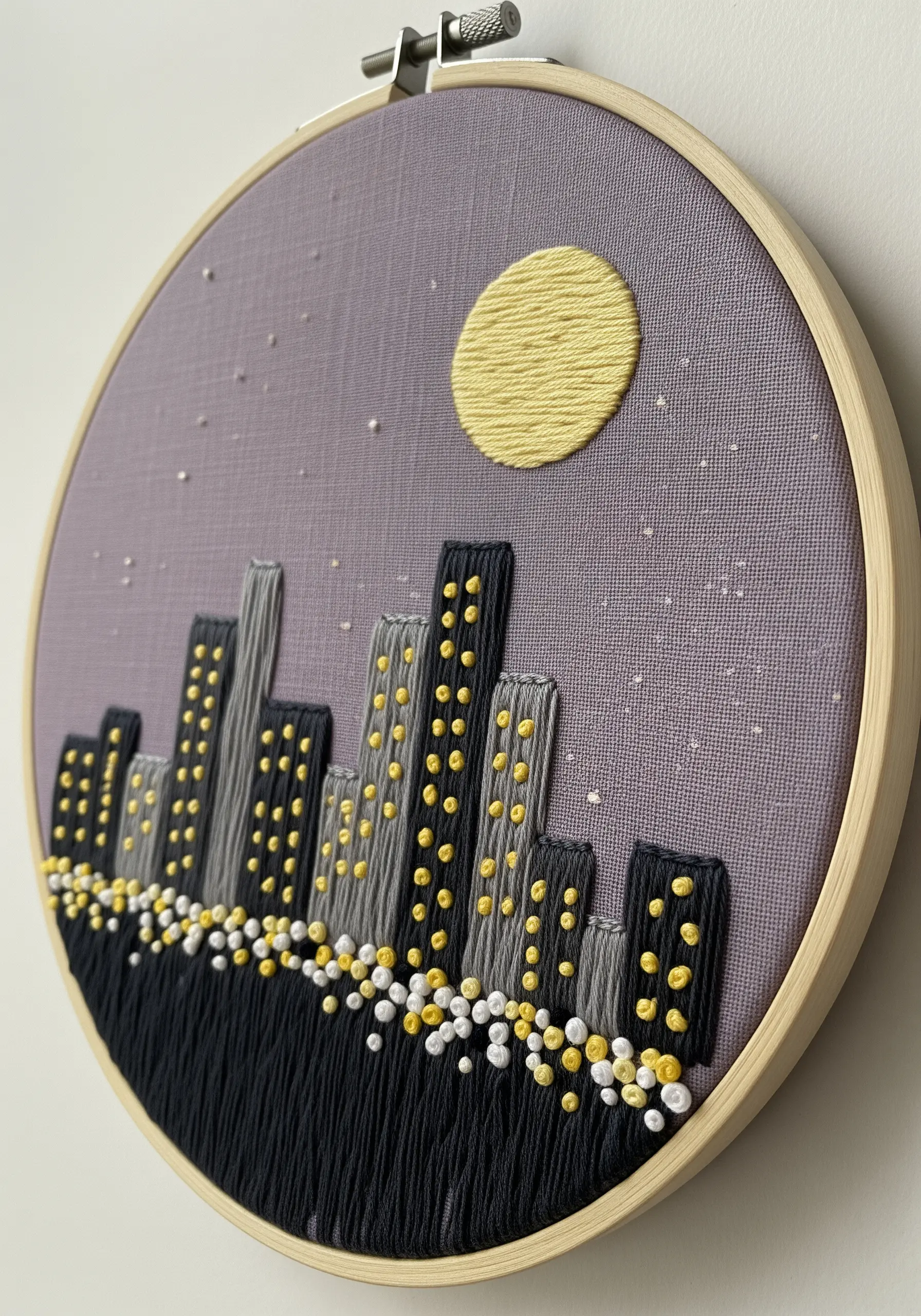 A cityscape at night with French knots used as glowing windows and streetlights.