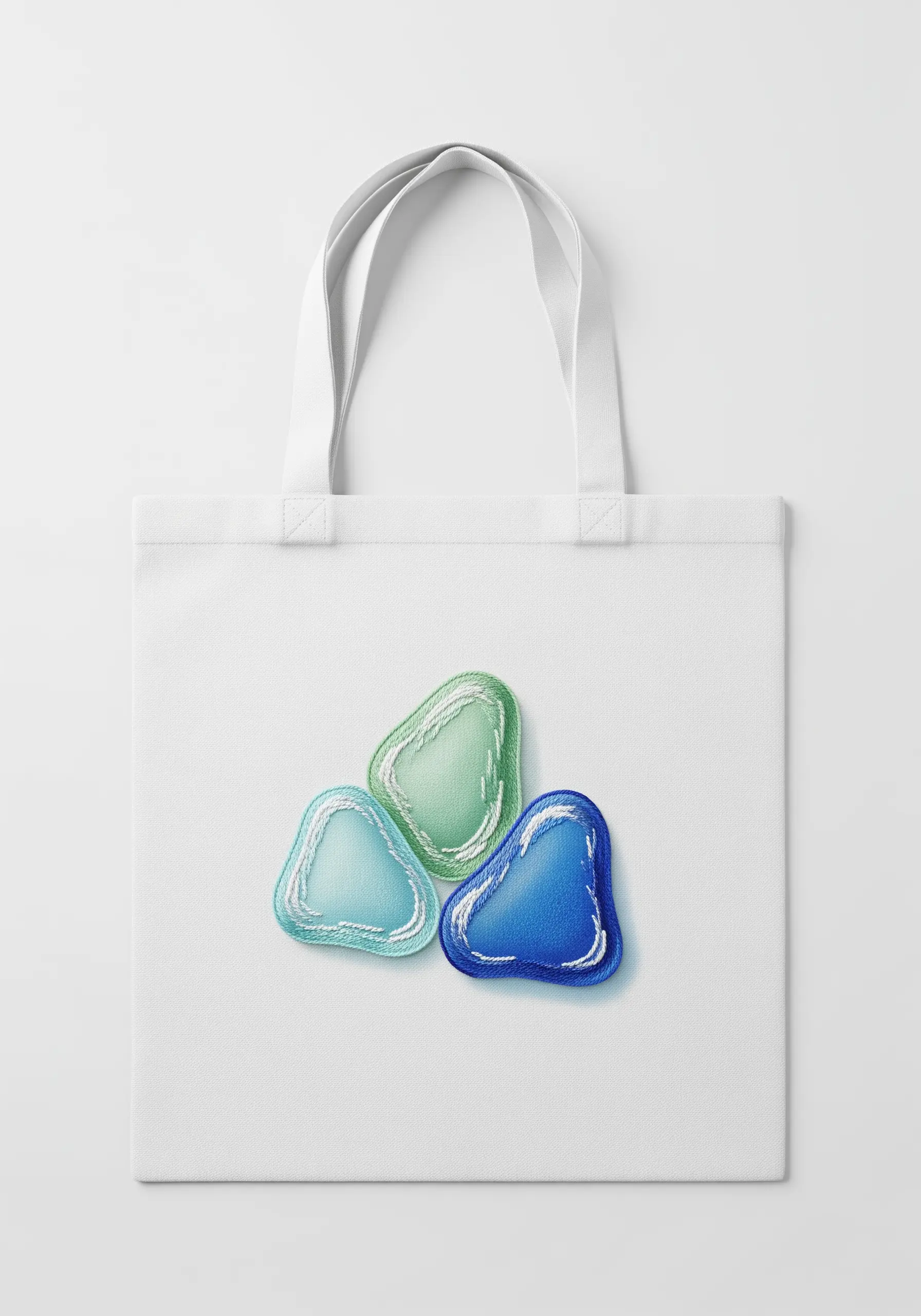 Three pieces of embroidered sea glass in blue and green, with a soft, frosted texture.