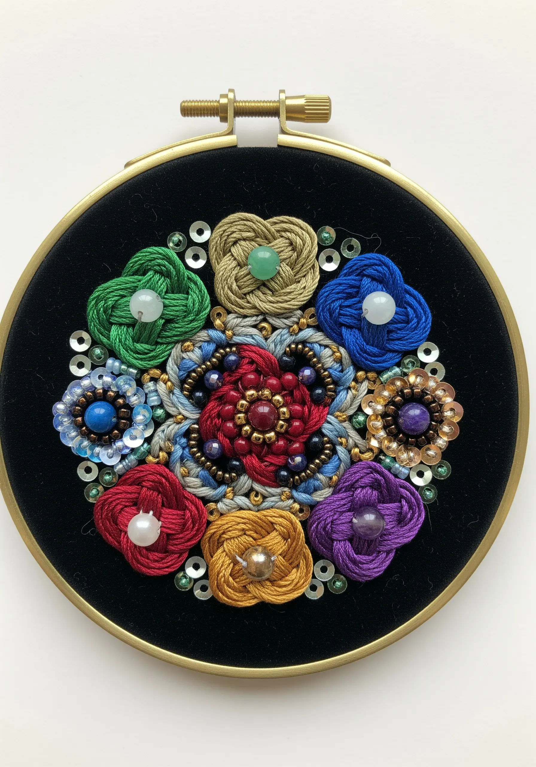 A small hoop with a colorful, beaded mandala featuring knotted floral shapes and sequins on black velvet.