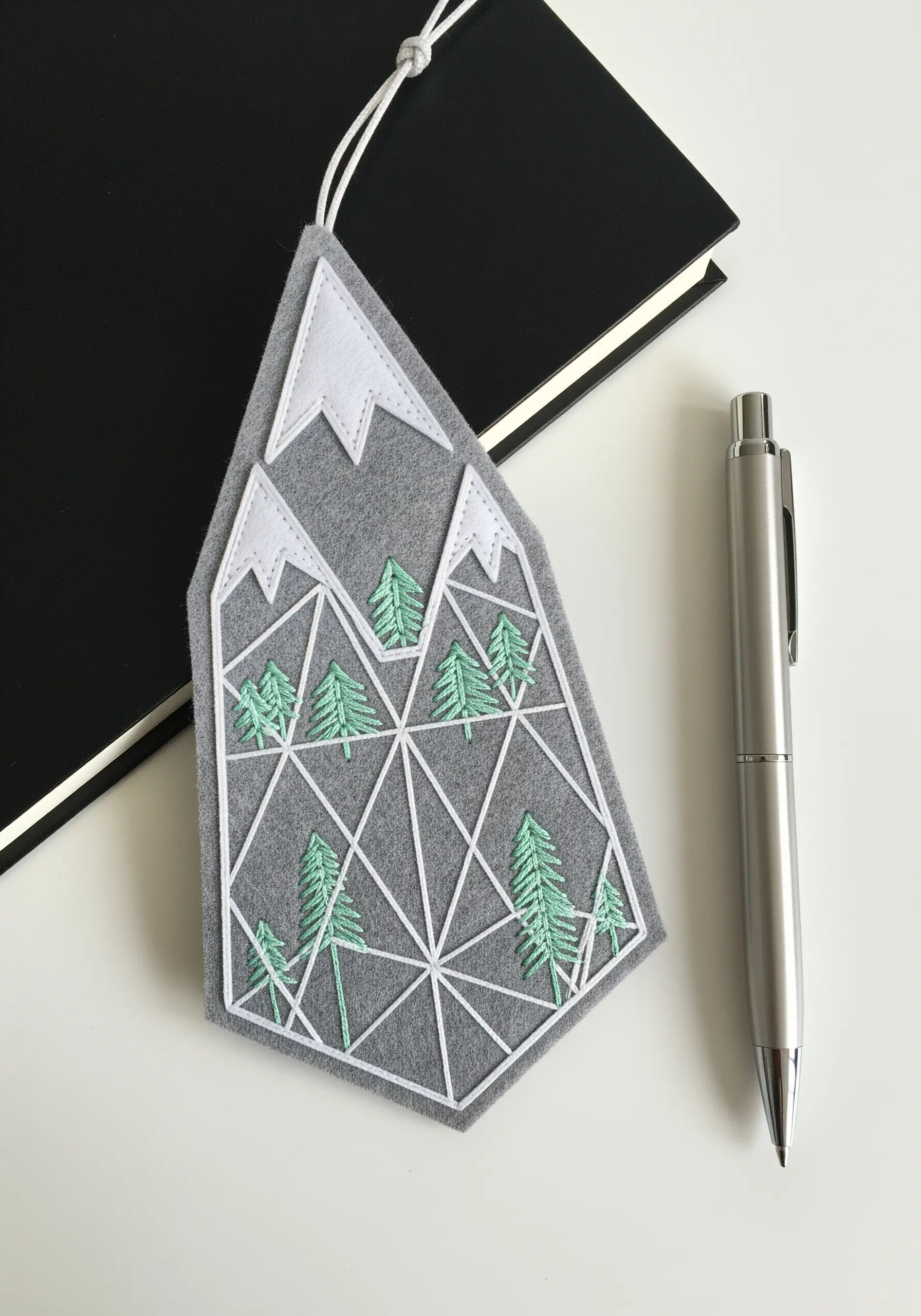 A geometric mountain-themed bookmark made from gray felt and white thread.