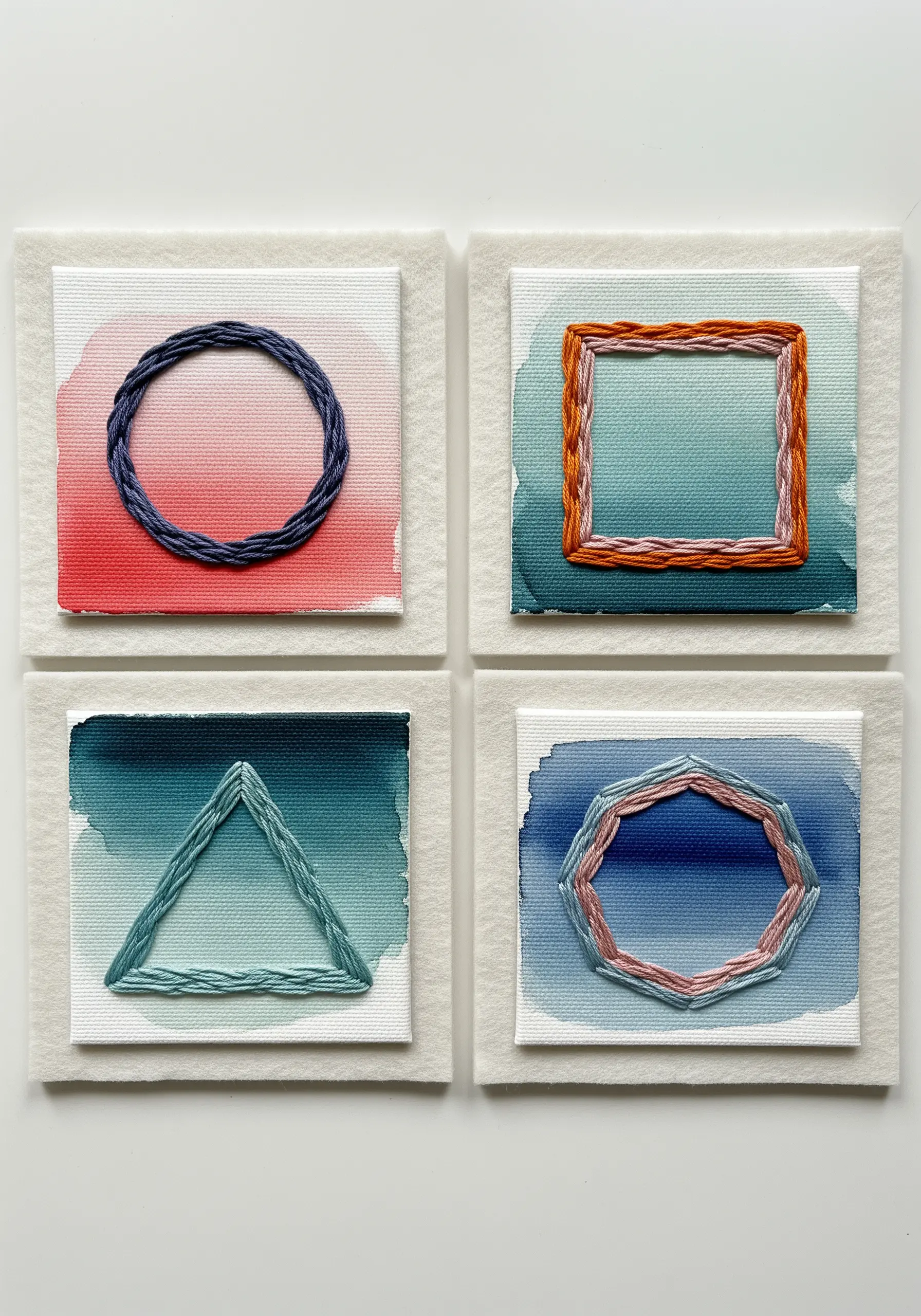 Four mini canvases with watercolor washes and embroidered geometric shapes in contrasting colors.