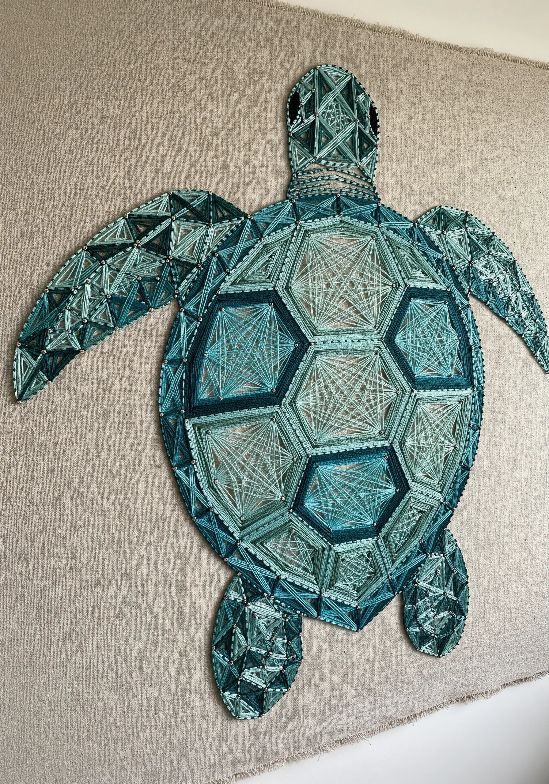 Geometric string art sea turtle on neutral linen, with a shell made of teal tessellated shapes.