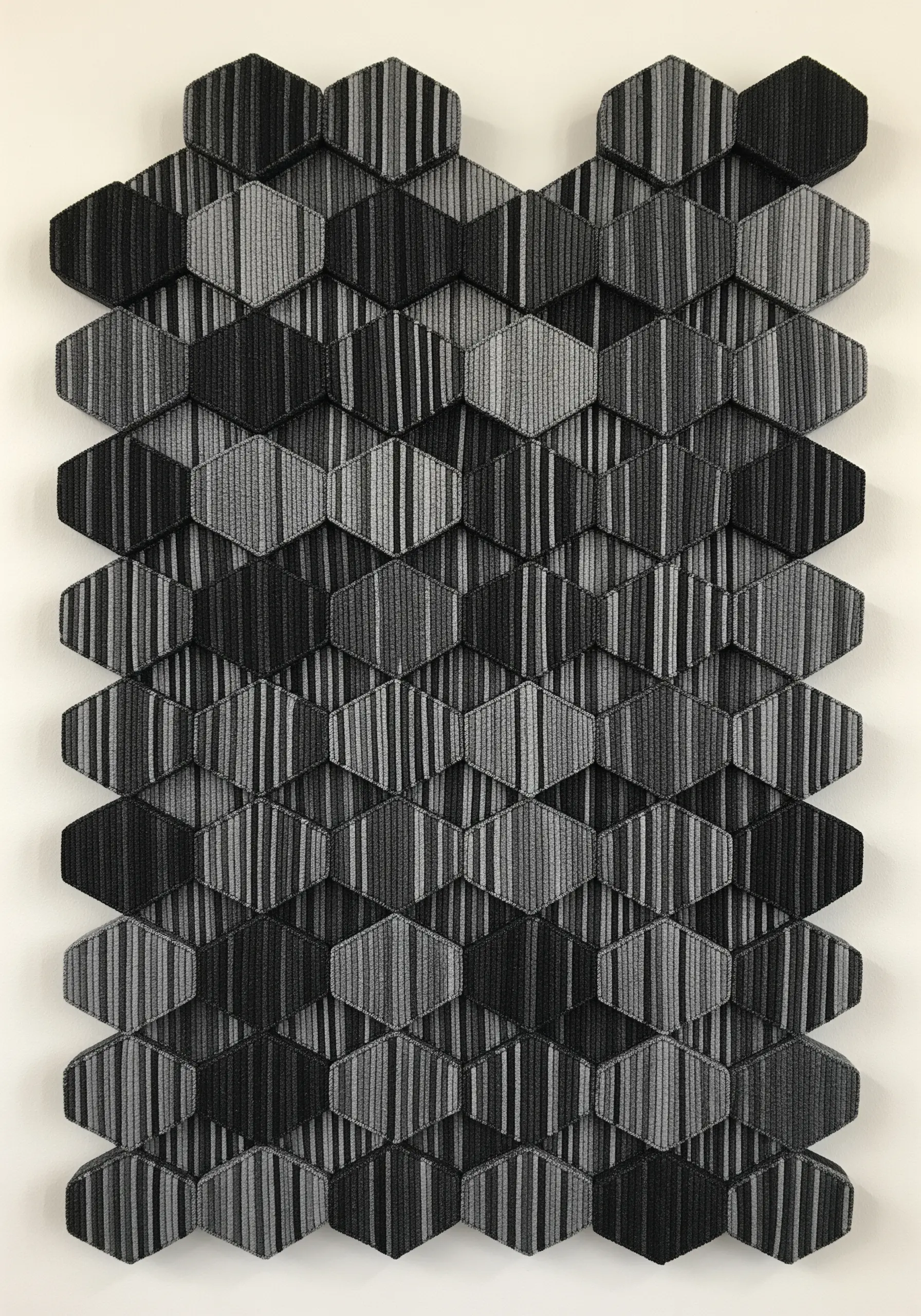 A geometric wall art piece made of individual embroidered hexagons in black and gray stripes.