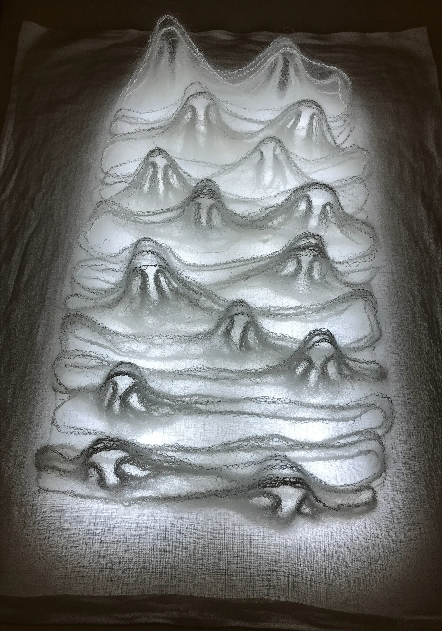 Ghostly white thread mountains stitched on layered sheer fabric and backlit.