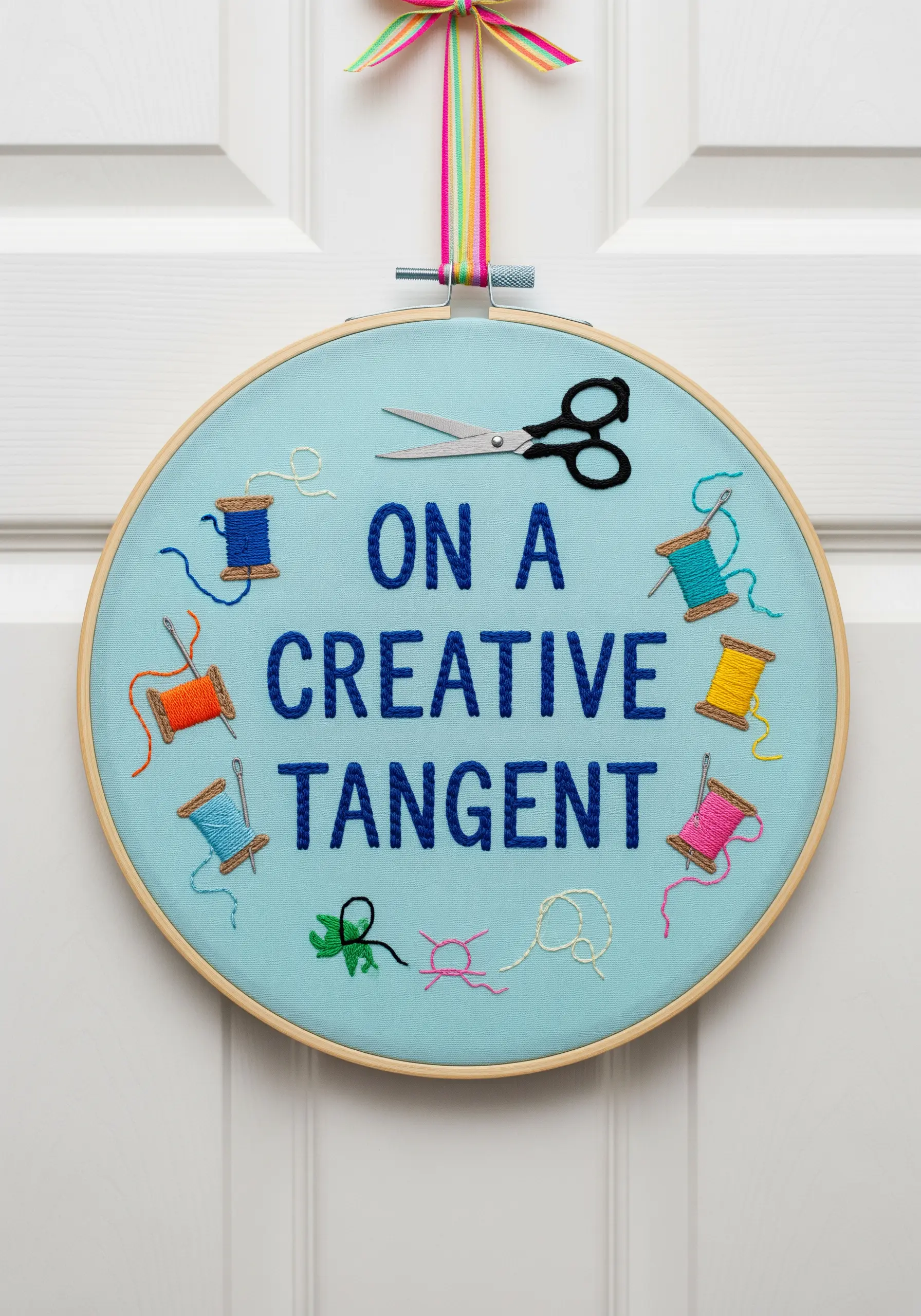 A blue embroidery hoop with the raised text 'On a creative tangent' and small thread spools.