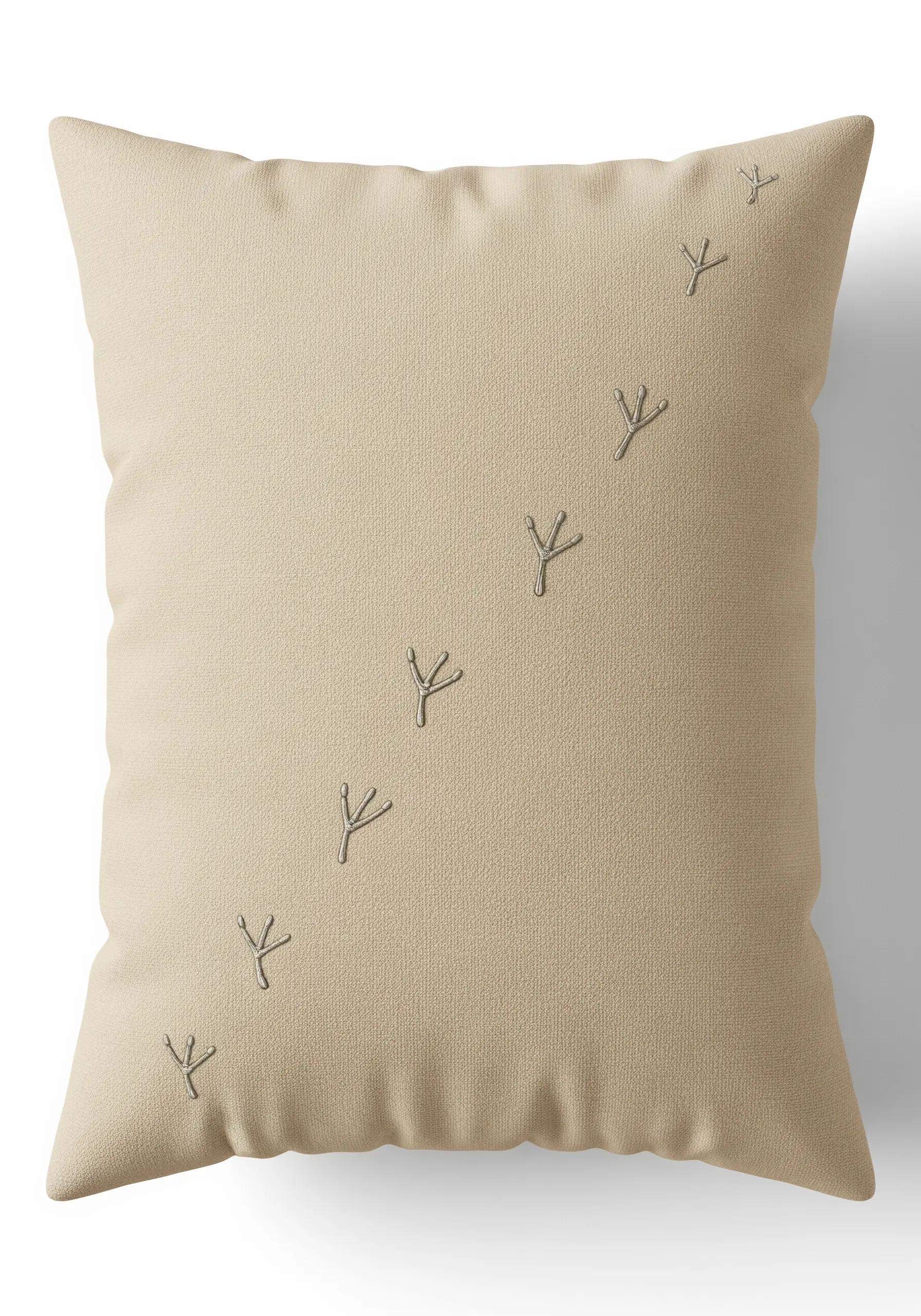 A diagonal line of tiny, embroidered bird footprints on a beige pillow