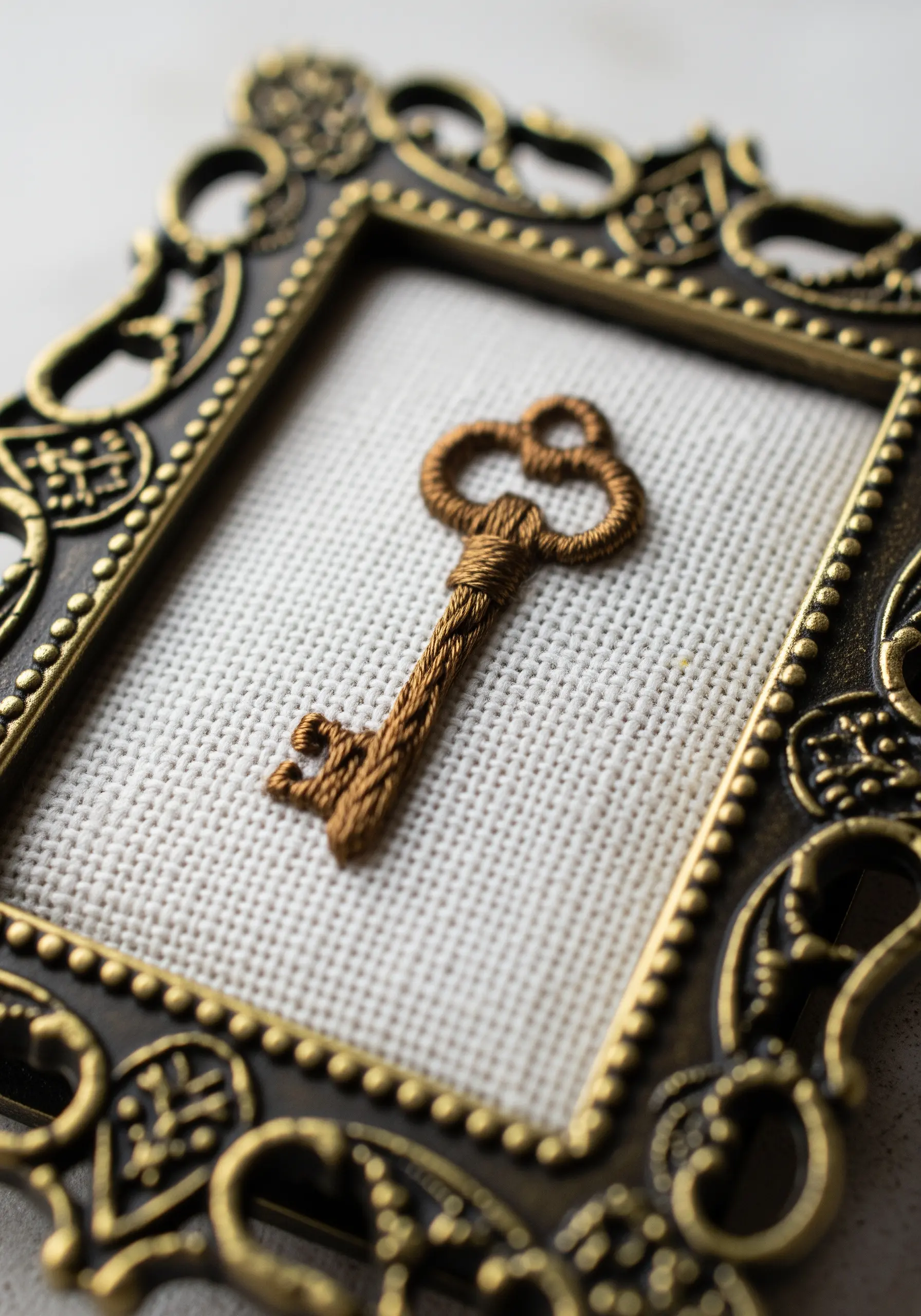 A 3D embroidered antique key with padded satin stitch in a vintage frame.