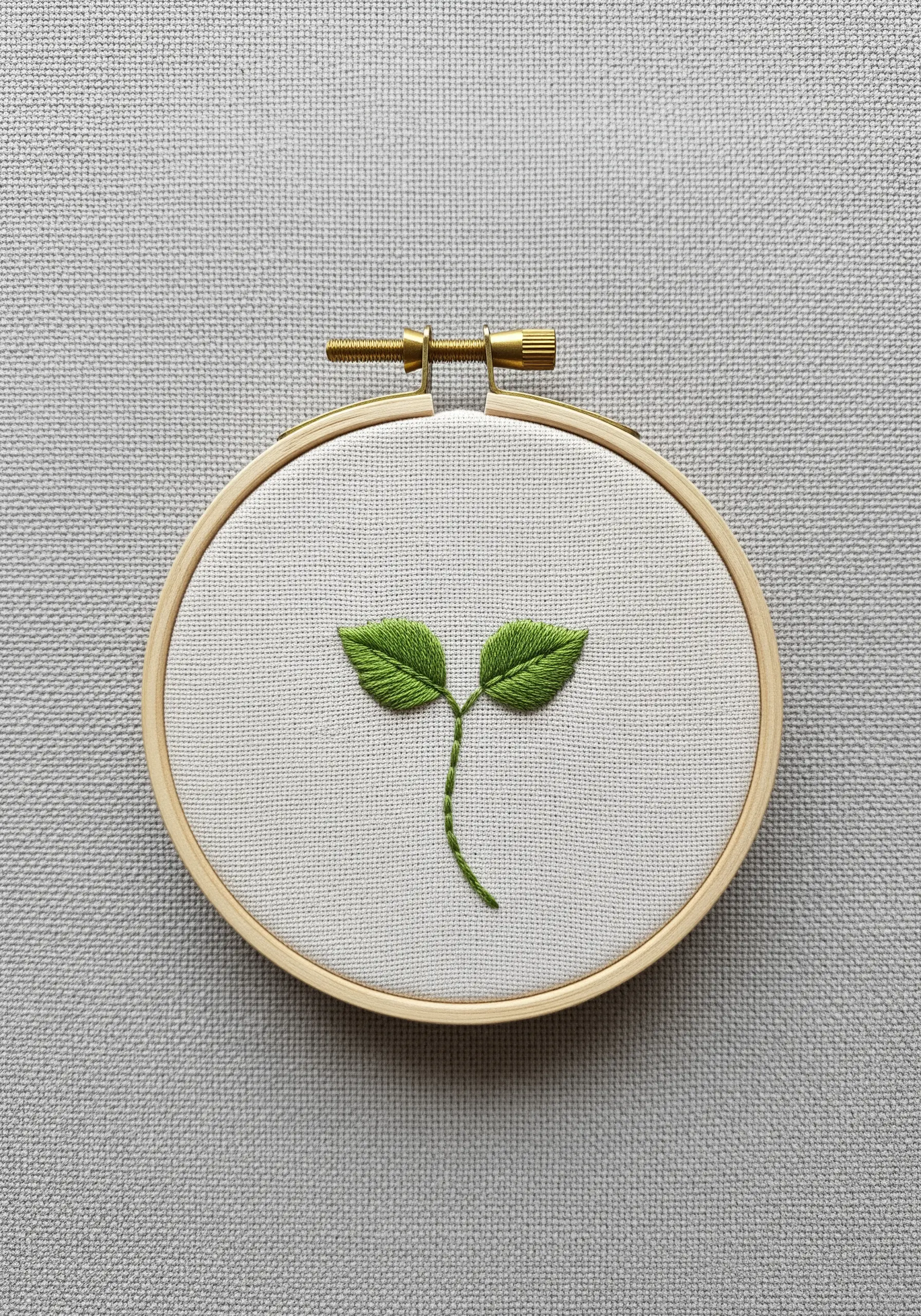 A small green sprout with two leaves embroidered using the fishbone stitch in a hoop.