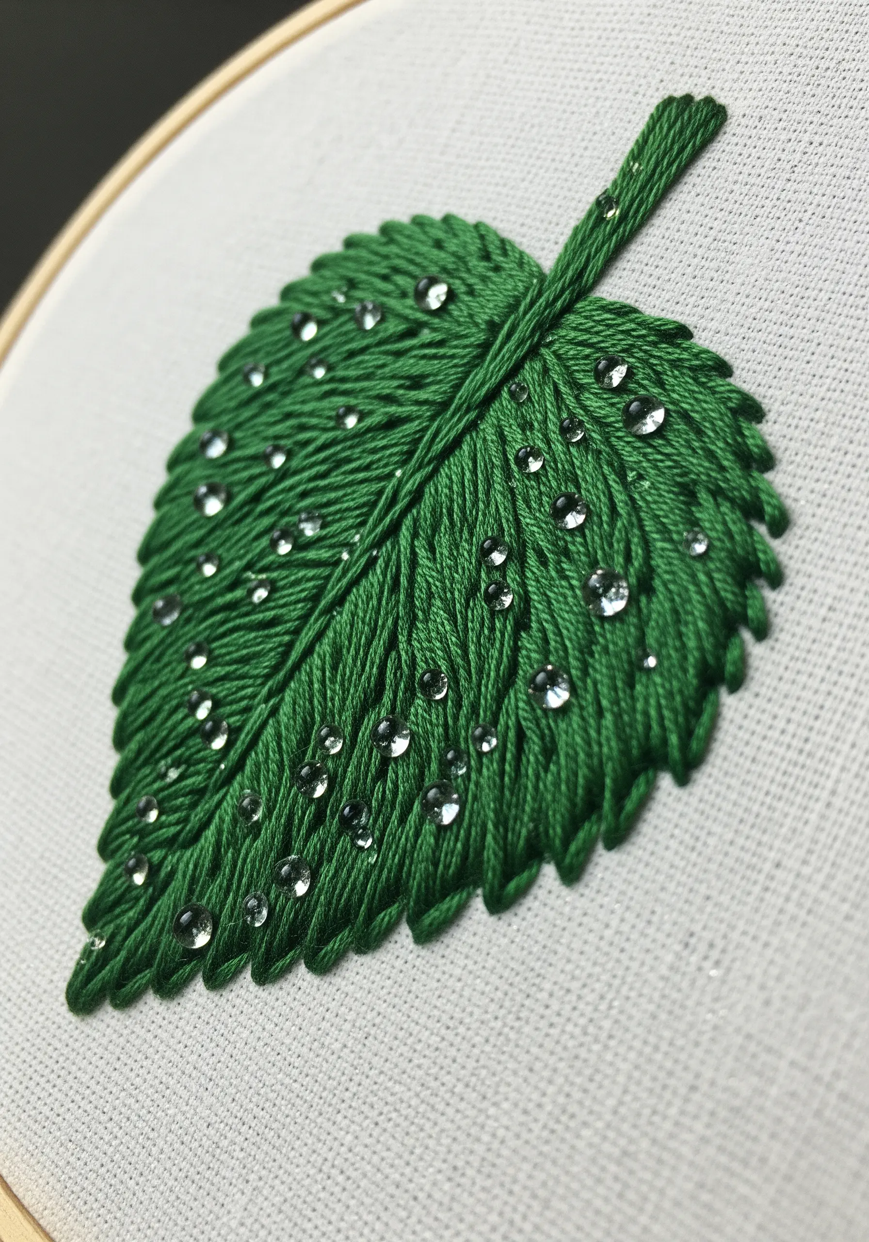 A satin-stitched green leaf embellished with small clear beads to look like water droplets.