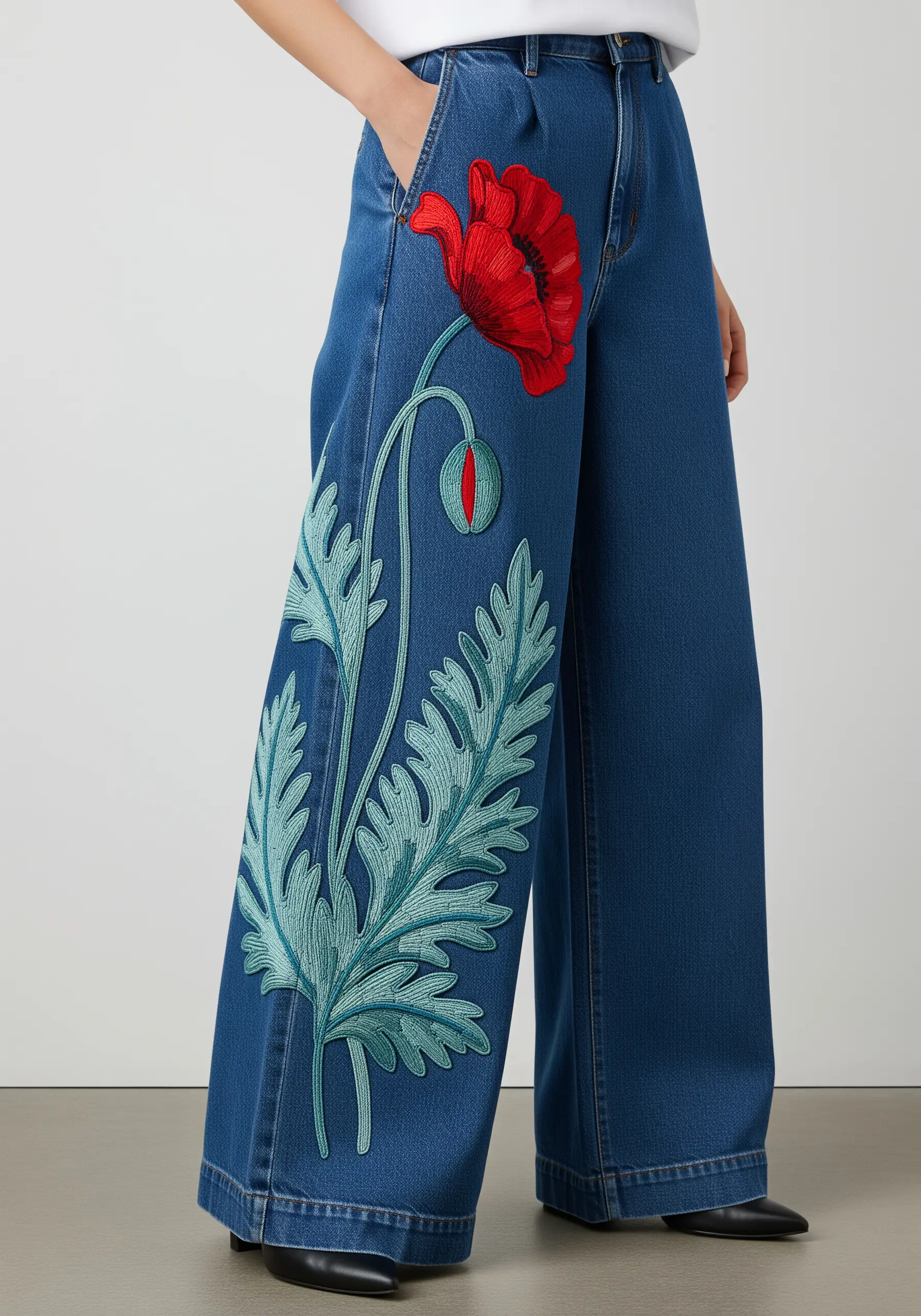 A large red poppy with long green leaves embroidered down the leg of wide-leg jeans.